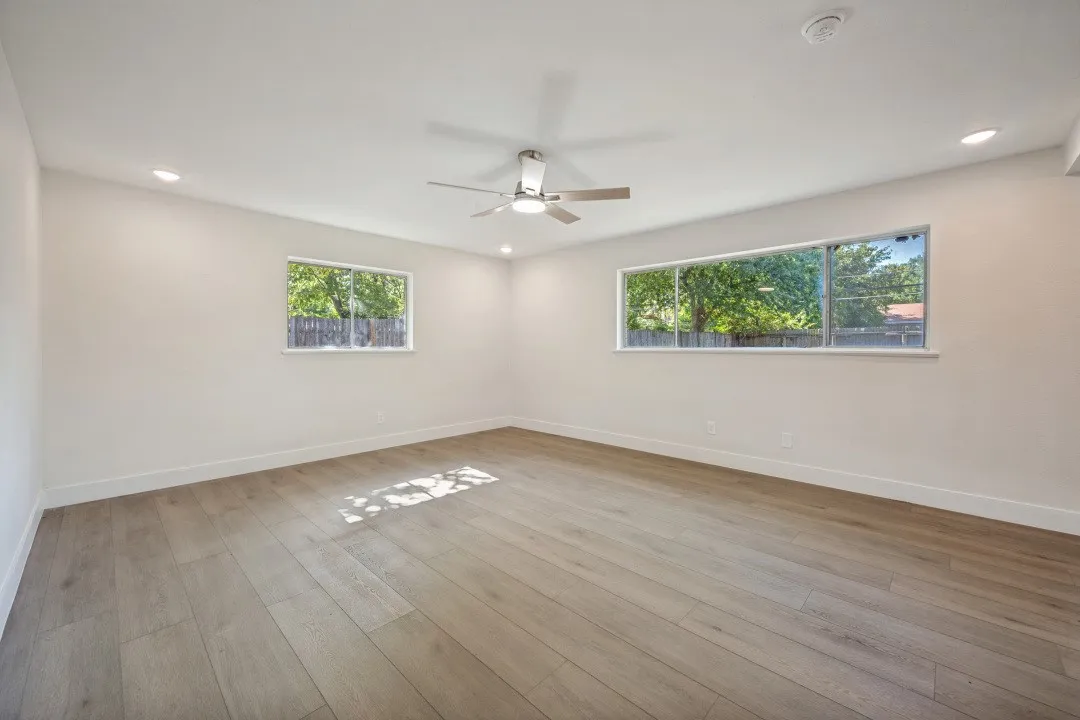 Spacious living area with large windows on two walls, a modern ceiling fan, recessed lighting, and abundant flexibility for multiple furniture arrangements.