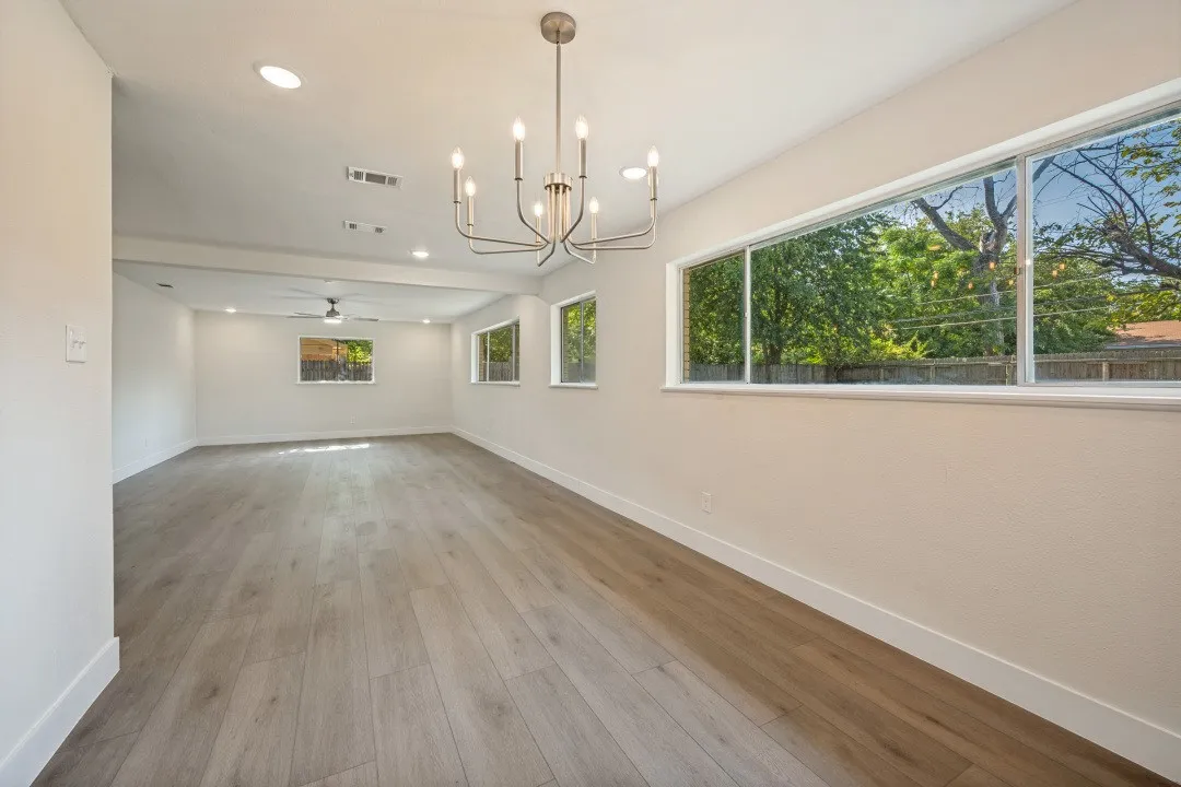 Light-filled dining space with contemporary chandelier, luxury vinyl plank flooring, and a dramatic row of oversized windows overlooking the surrounding trees and backyard.