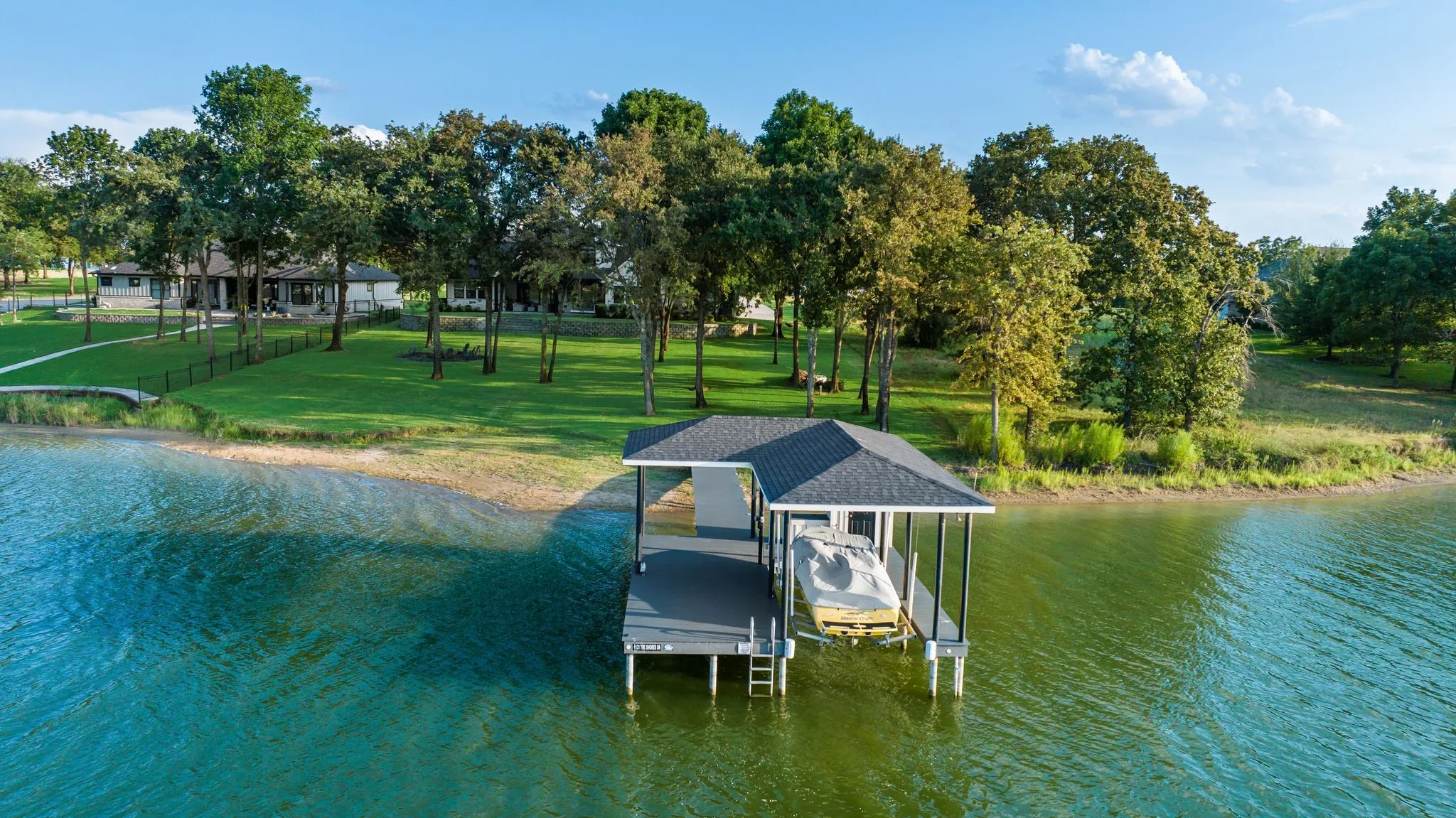 Spacious and shaded by mature trees, the lawn expands to the shoreline.