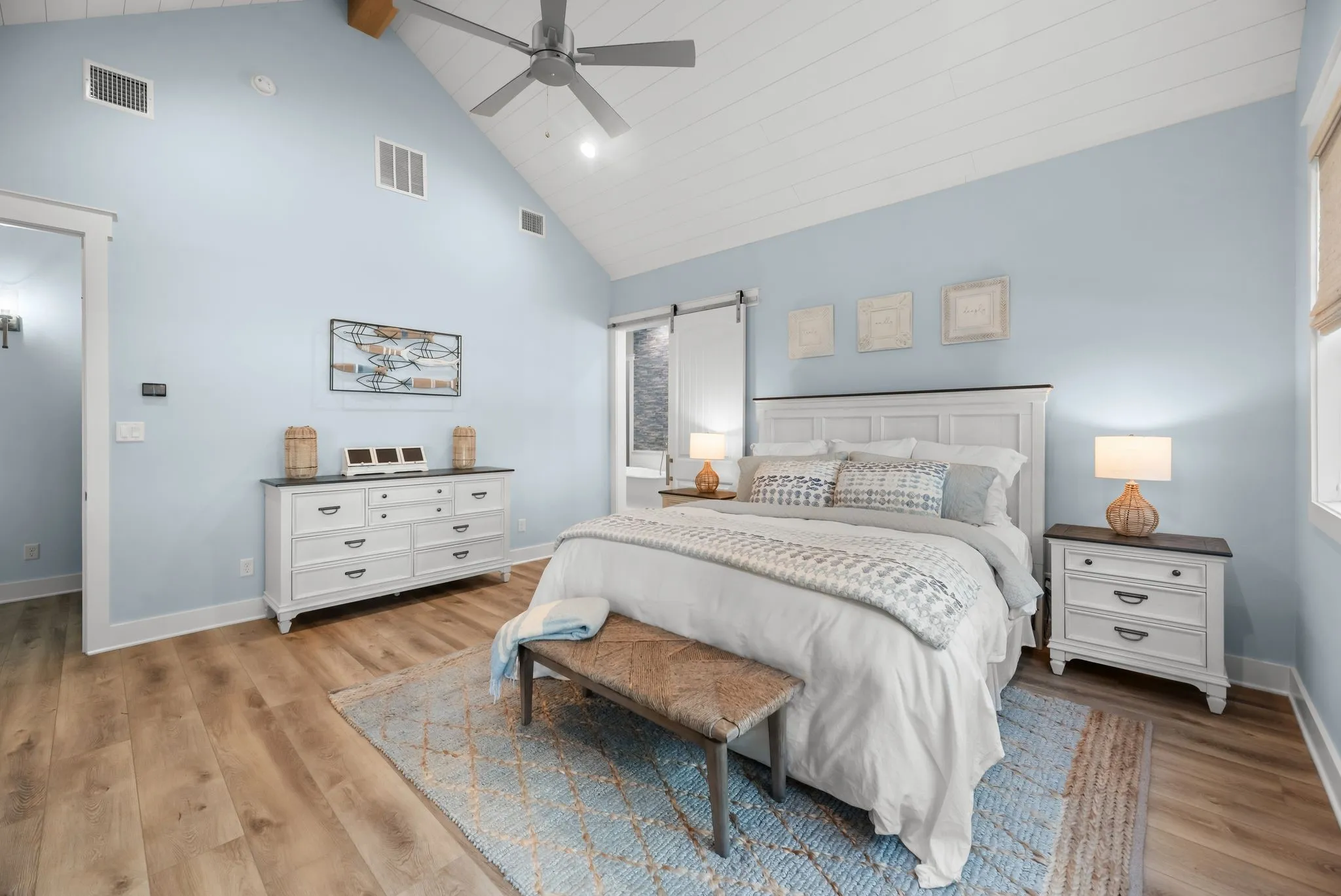 Luxurious primary bedroom combines modern farmhouse style, hard-surface flooring, ceiling fan, and ample space for a private sitting area.