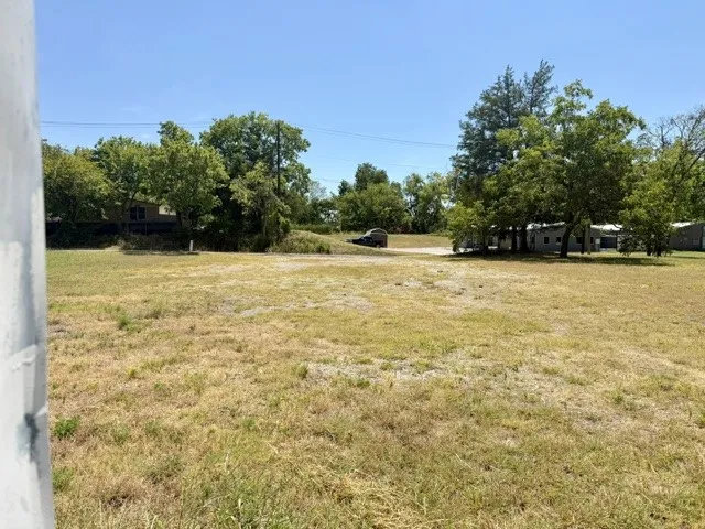 Expansive open lot with natural surroundings, mature trees, and a clear sky backdrop