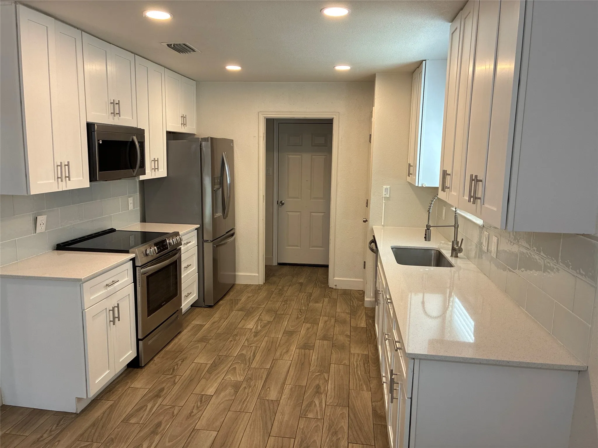 White cabinetry, stainless steel appliances, light-toned countertops, subway tile backsplash, and wood-finish flooring