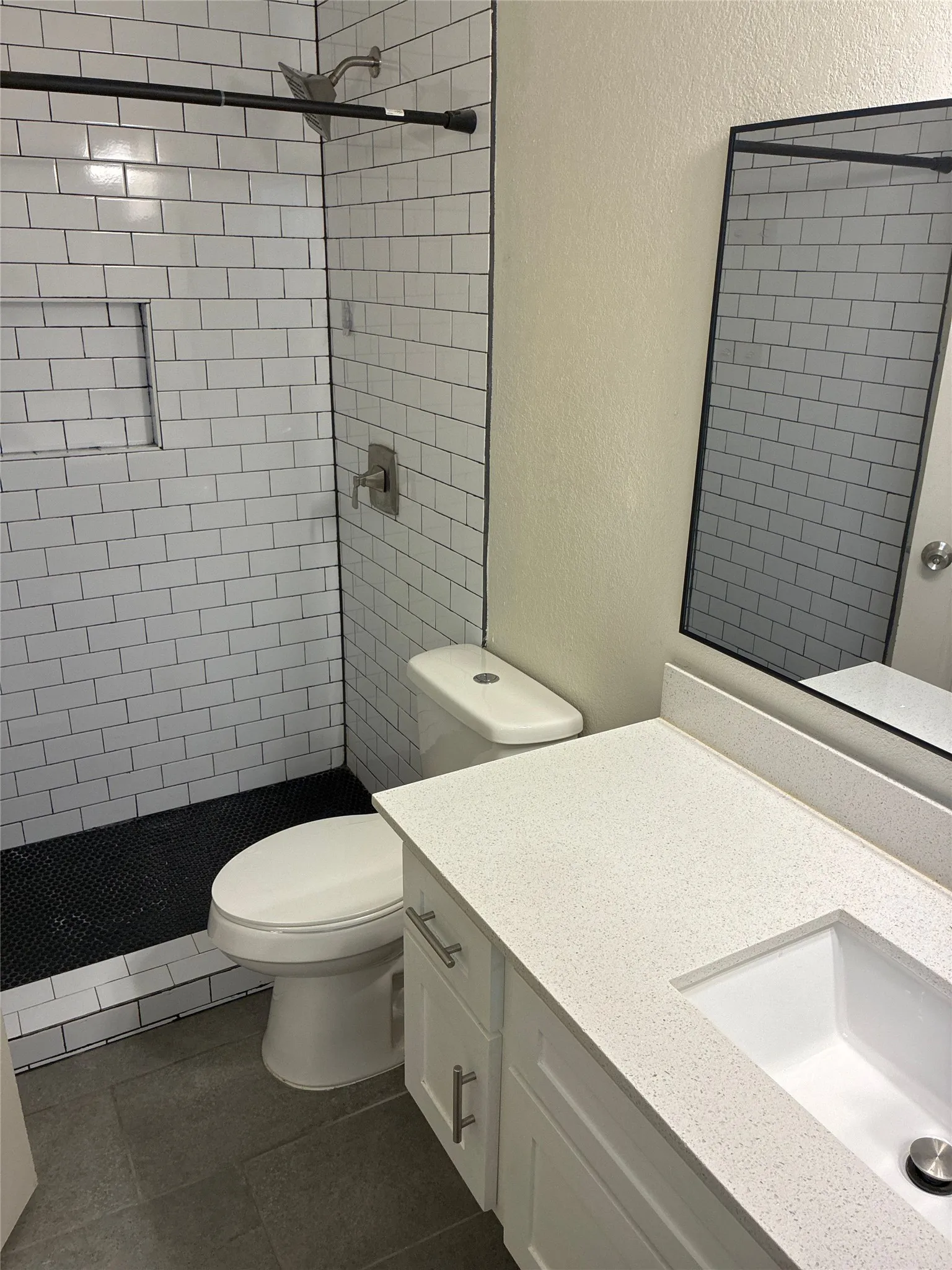 White subway tile shower with a built-in niche, featuring a black mosaic shower pan