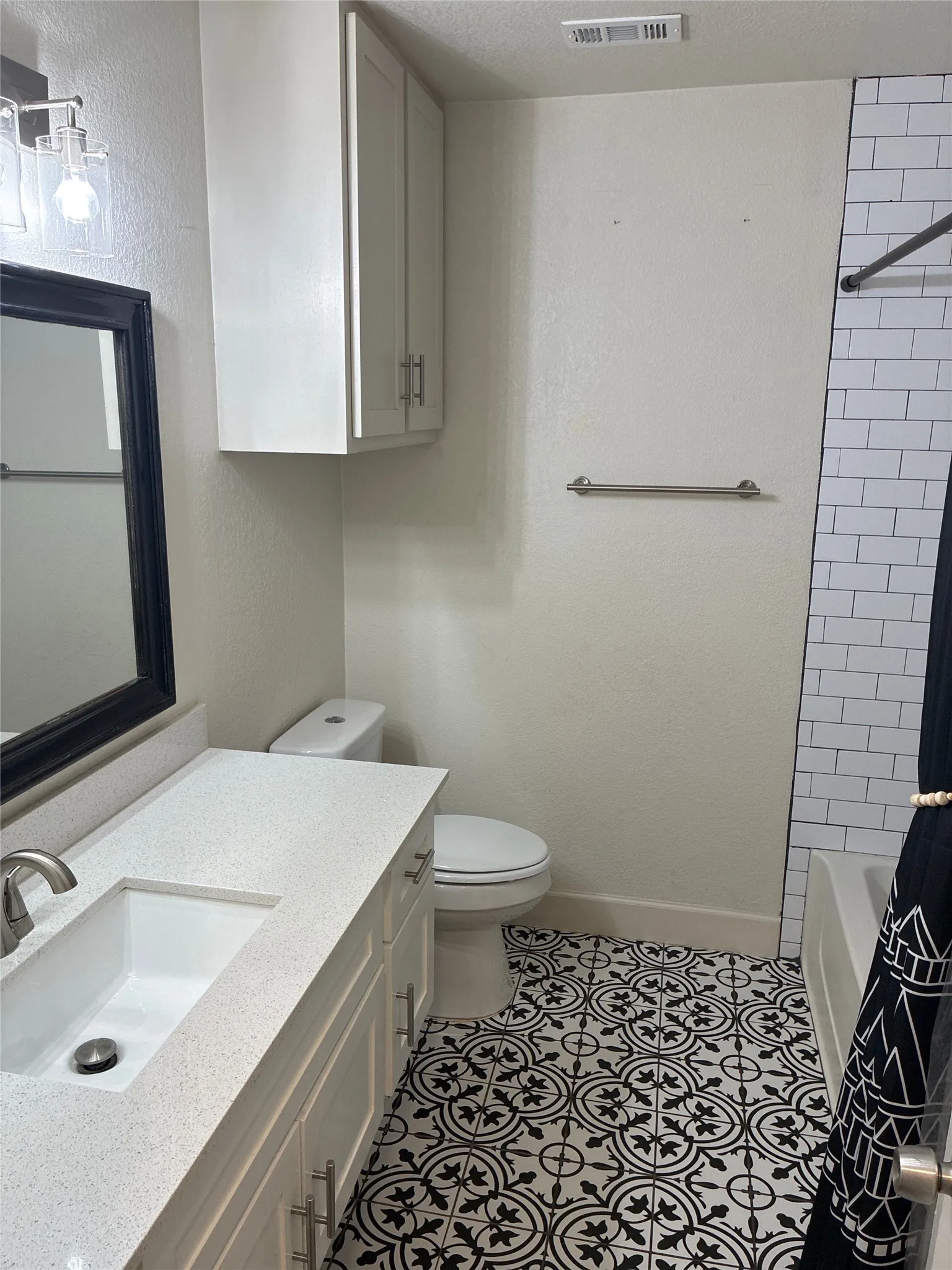 Vanity with integrated sink and chrome faucet, white cabinetry, decorative floor tiling, subway tile shower surround, and a wall-mounted medicine cabinet