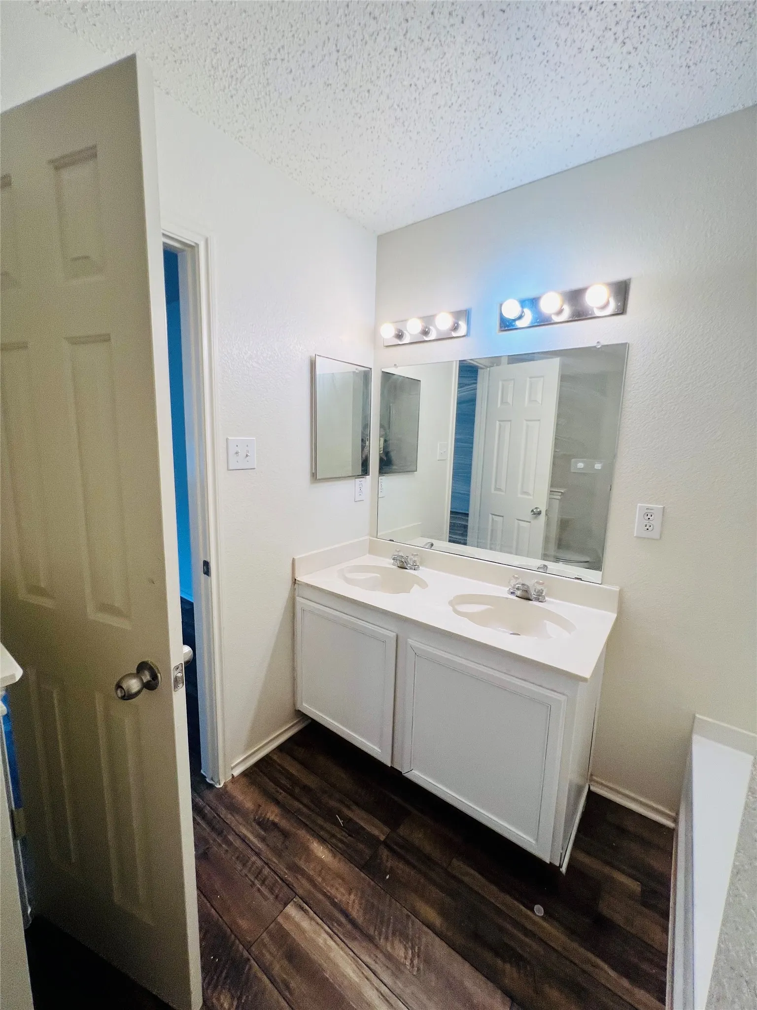 Dual sink vanity with white cabinetry, integrated white countertops, and wood-finish flooring