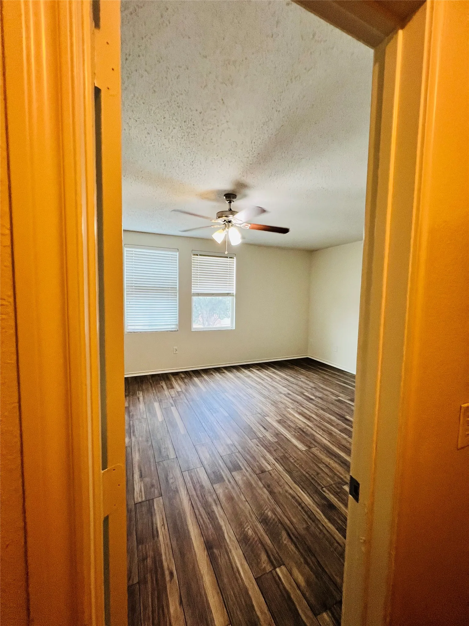 Spacious room featuring wood-finish flooring, two windows with blinds, and a ceiling fan with integrated lighting