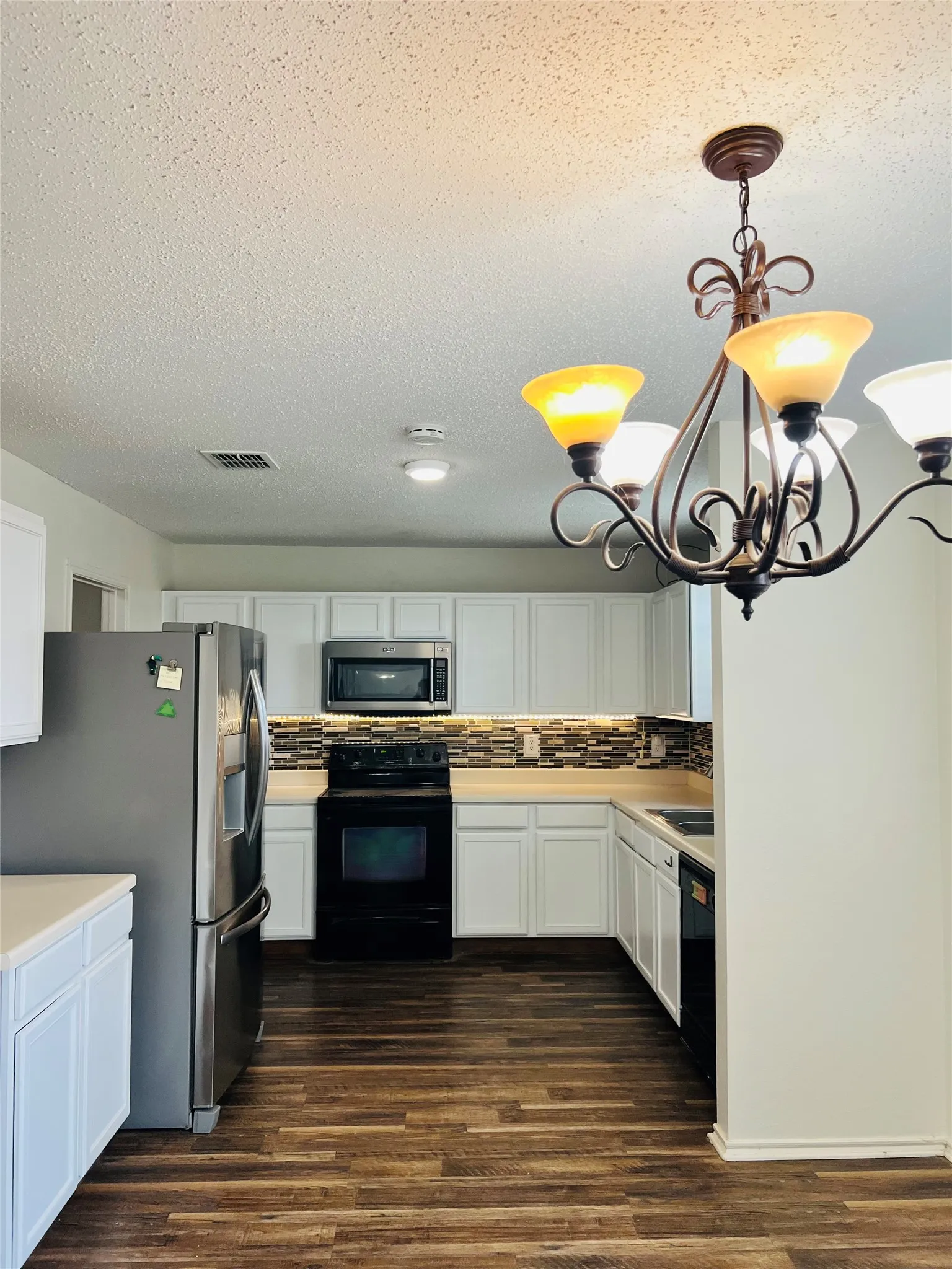 Kitchen featuring wood-finish flooring, white cabinetry, a mosaic tile backsplash, stainless steel refrigerator, and a dark finish range
