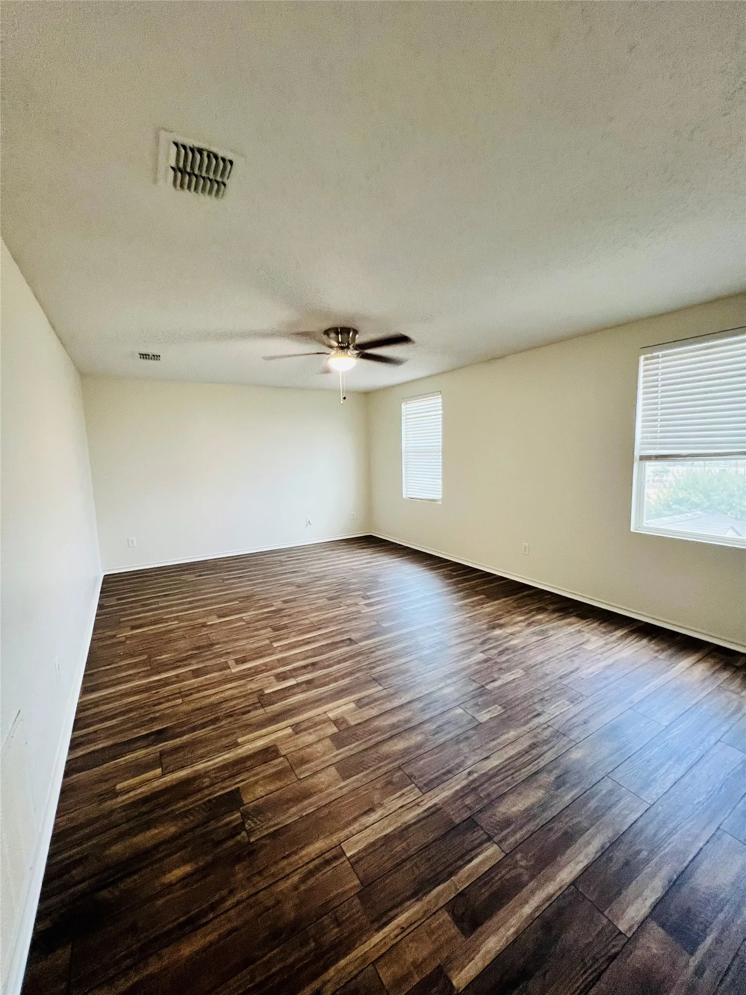 Expansive room featuring wood-finish flooring, two windows with blinds, and a ceiling fan
