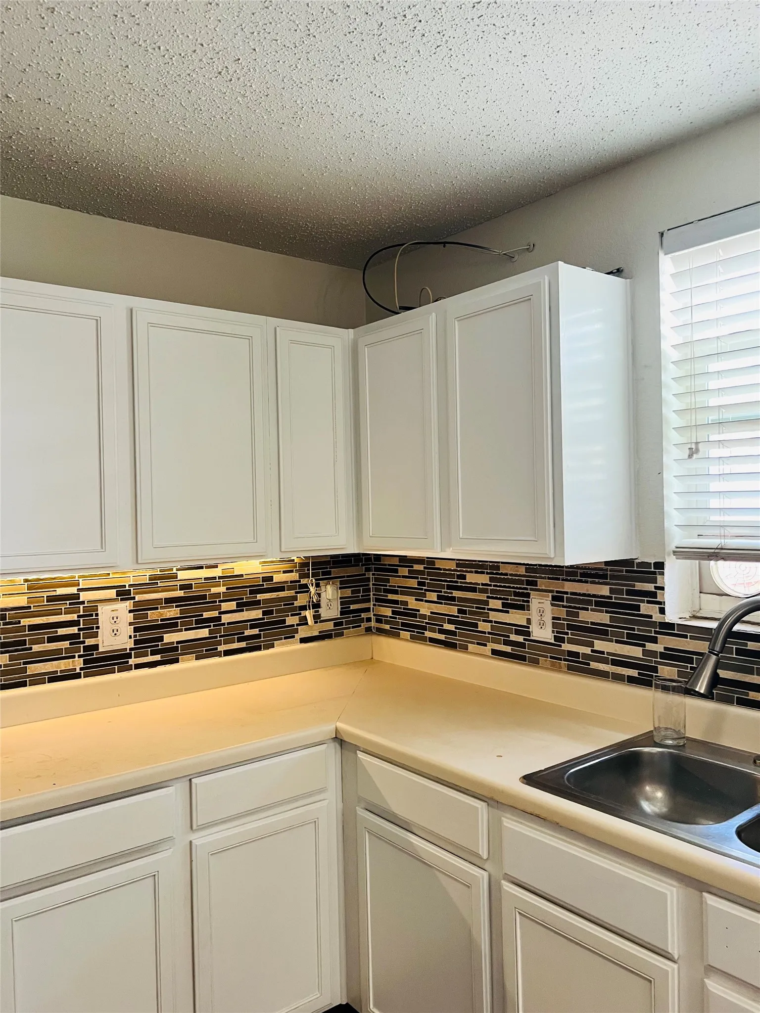 White shaker-style cabinetry, mosaic tile backsplash, solid surface countertops, and a stainless steel double basin sink