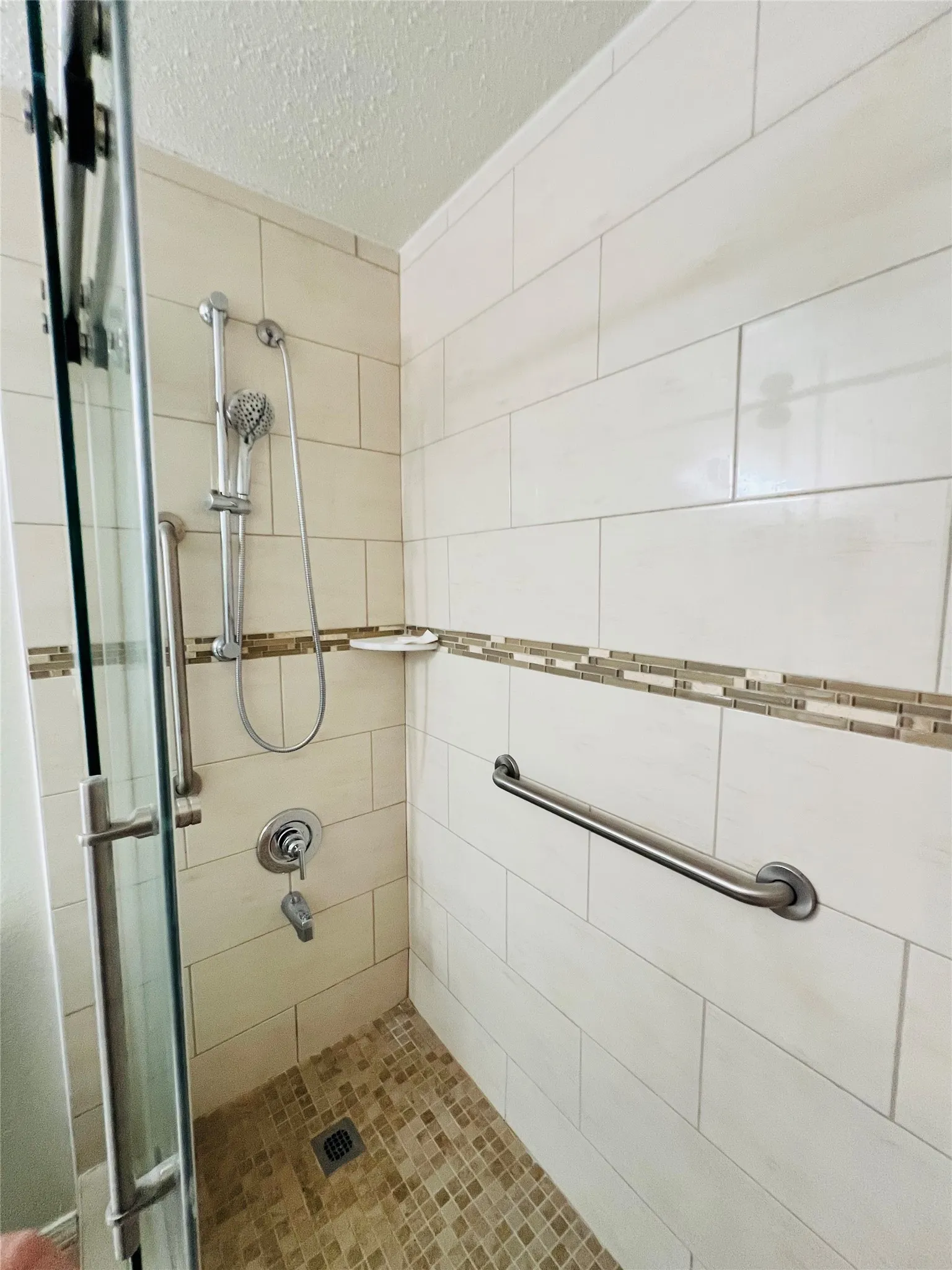 Tiled shower enclosure featuring a mosaic floor, a decorative tile accent band, and a glass shower door