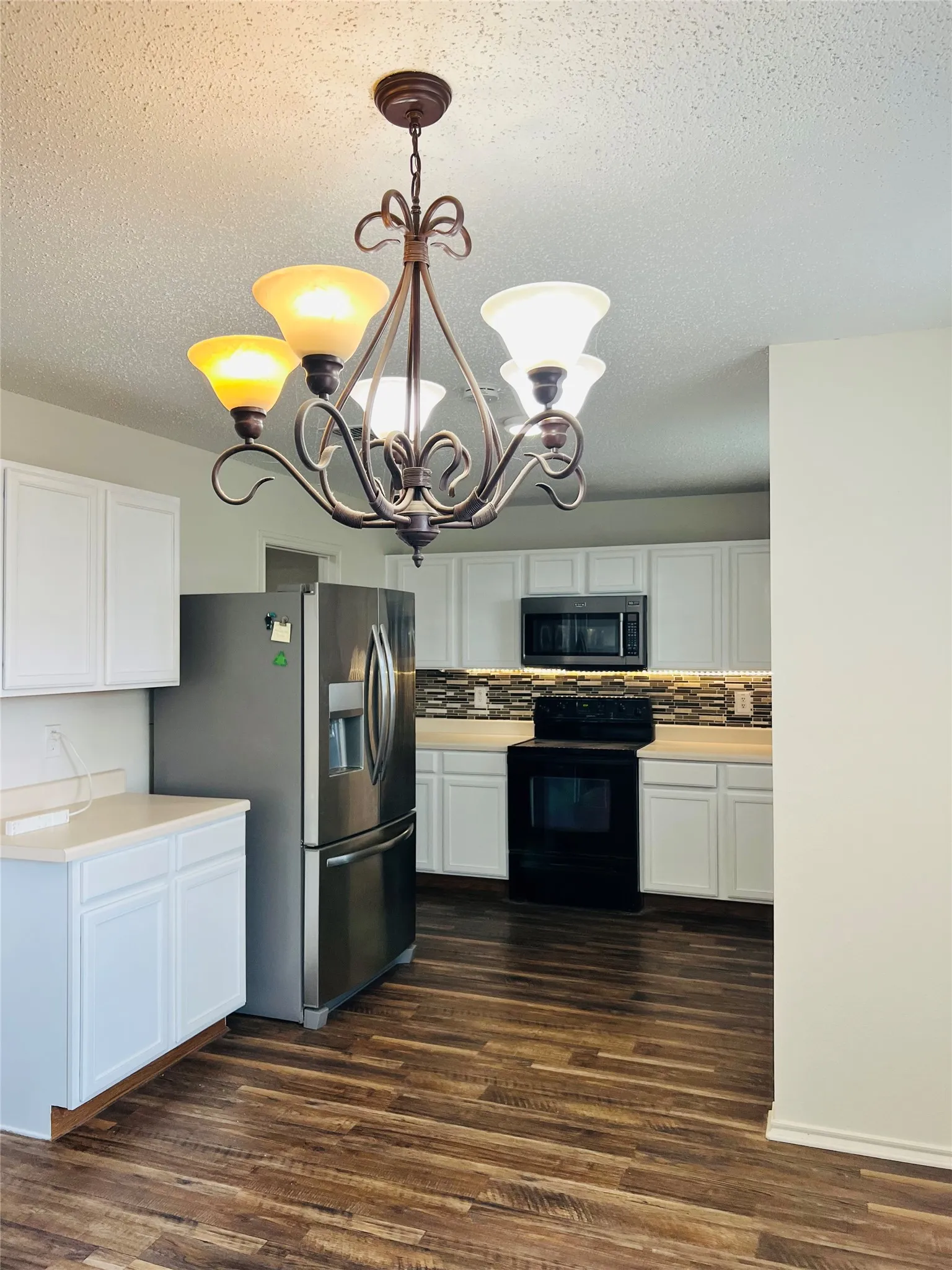 Kitchen featuring wood-finish flooring, white cabinetry, dark tile backsplash, and a decorative chandelier