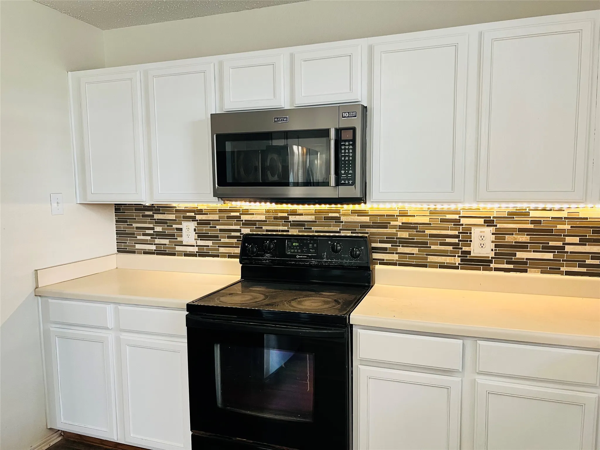 White cabinetry, stainless steel microwave, mosaic tile backsplash, countertop space, and electric range