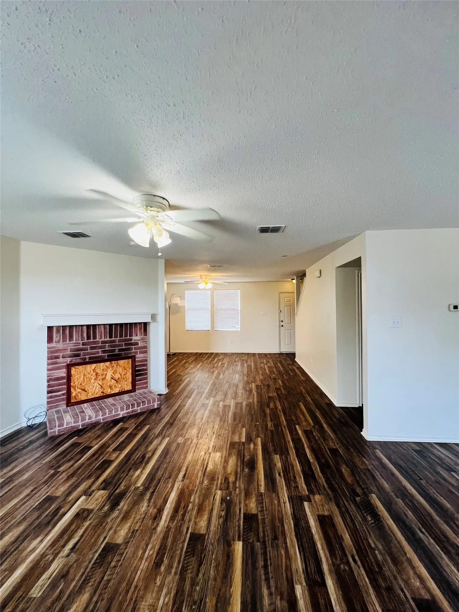 Wood-finish flooring throughout, brick fireplace with white mantel, ceiling fans with integrated lighting, and multiple windows