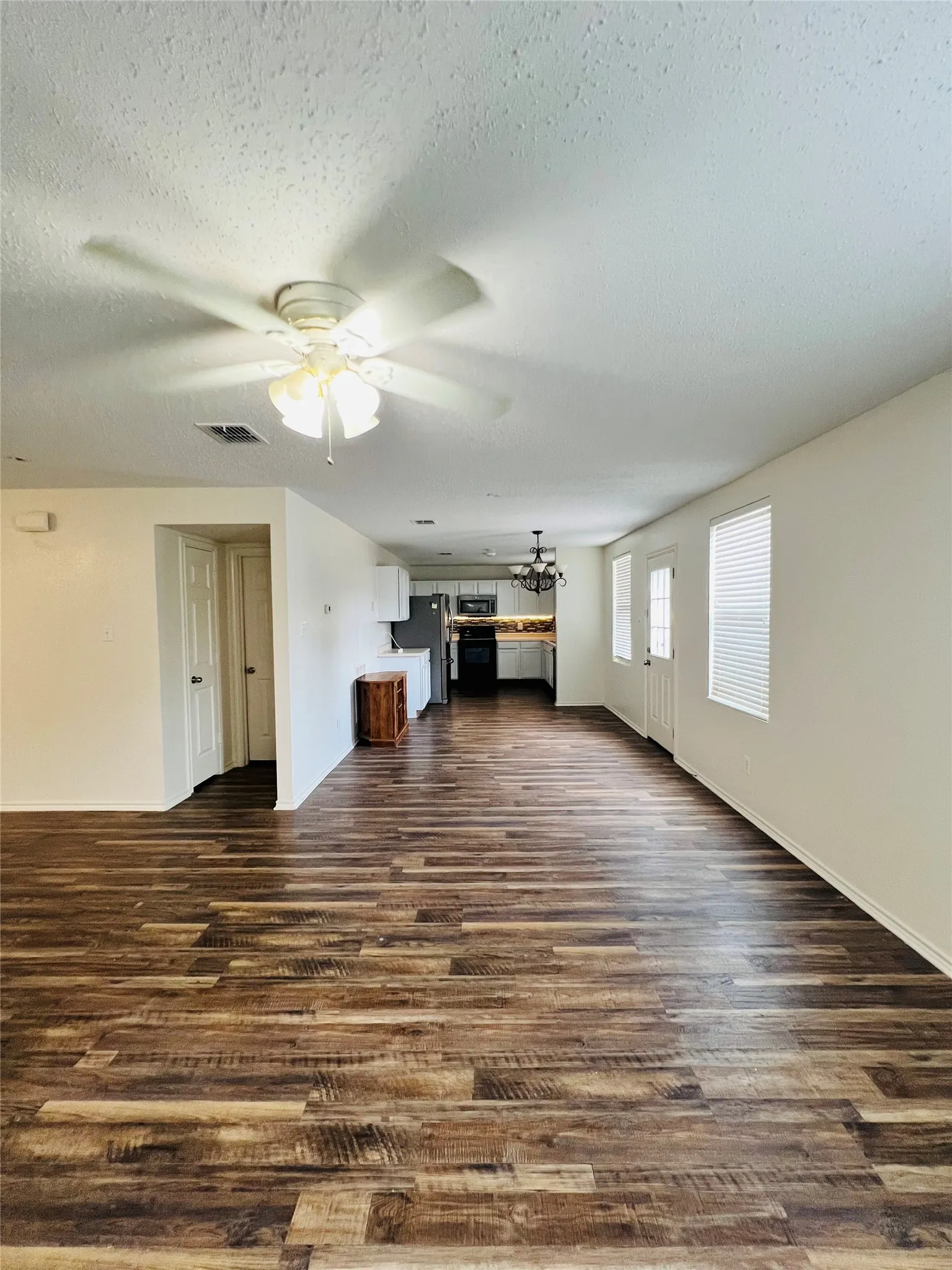 Wood-finish flooring throughout, white walls, ceiling fan with integrated lighting, window with blinds, and white interior doors