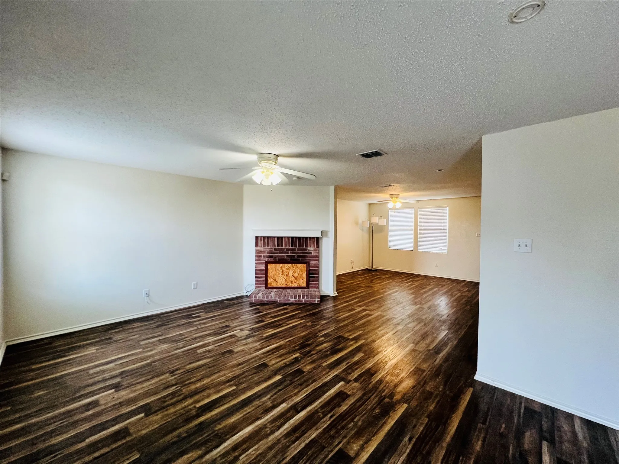 Spacious living area featuring wood-finish flooring, a brick fireplace with a white mantel, and ceiling fans
