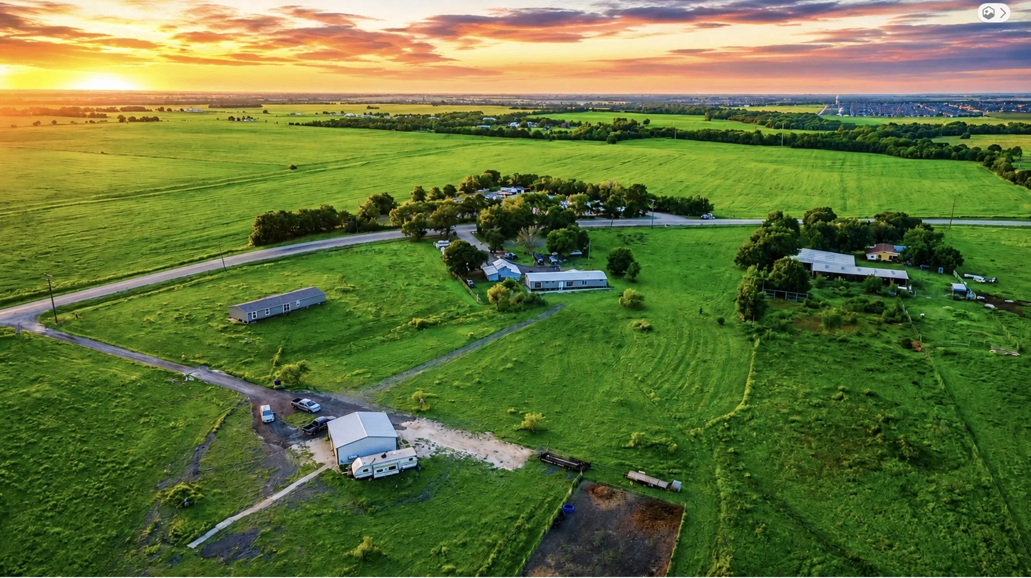 Expansive rural property featuring lush pastureland, mature tree clusters, and multiple outbuildings including a large agricultural structure