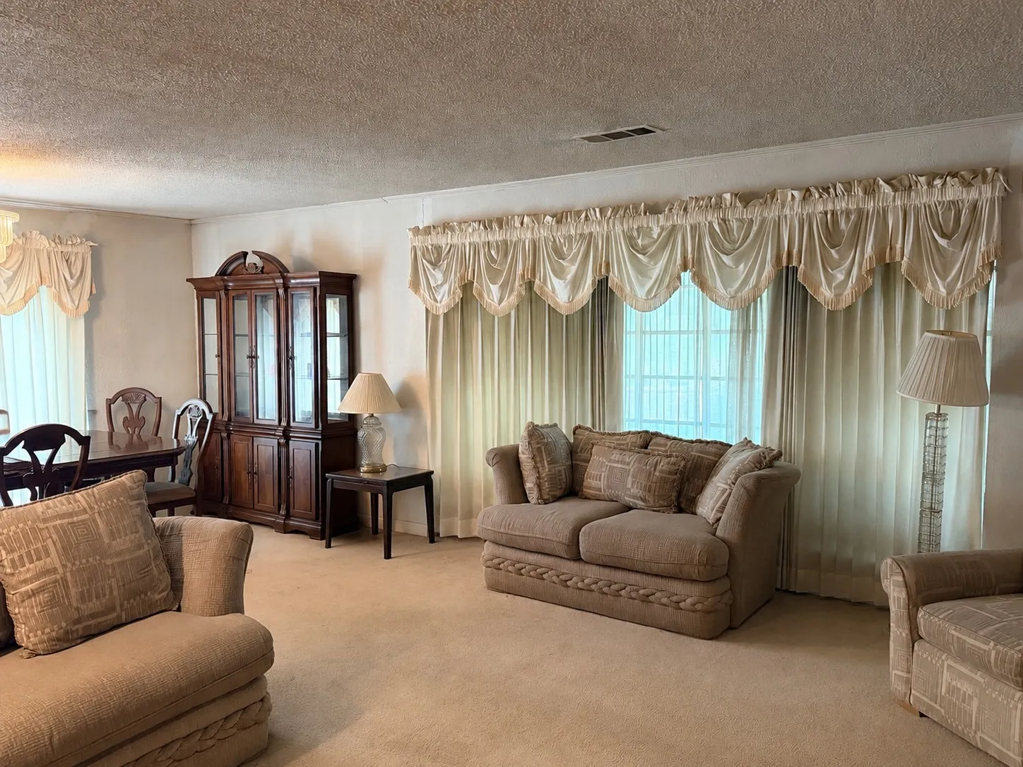 Expansive carpeted flooring, large window with vertical blinds, and a built-in wood display cabinet