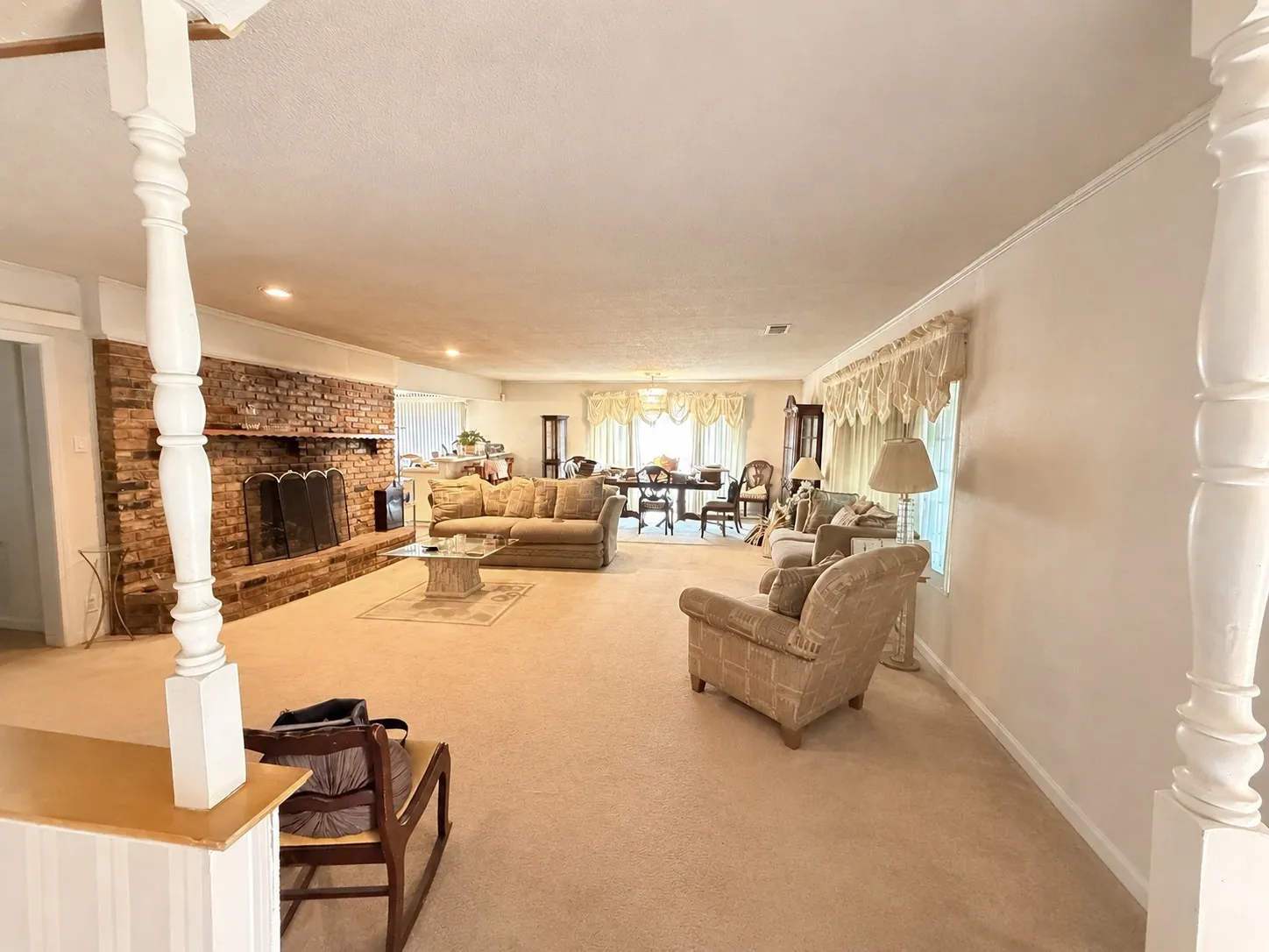 Spacious living area featuring a prominent brick fireplace, carpeted flooring, and decorative interior columns