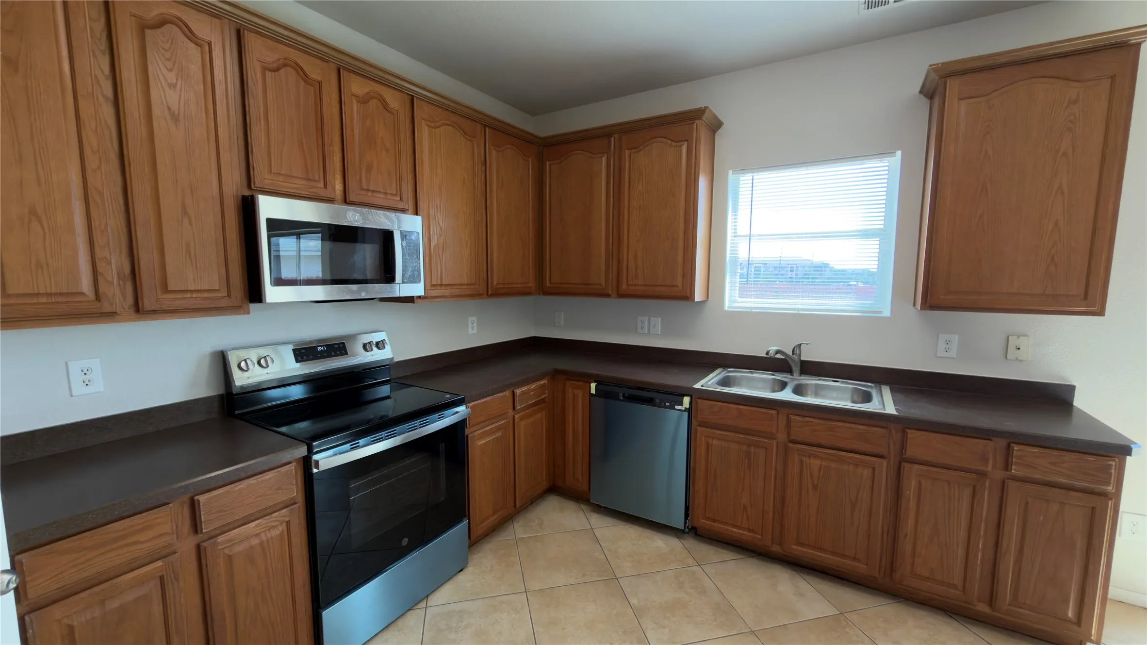 Kitchen featuring wood cabinetry, stainless steel appliances, a dual basin sink, and tile flooring