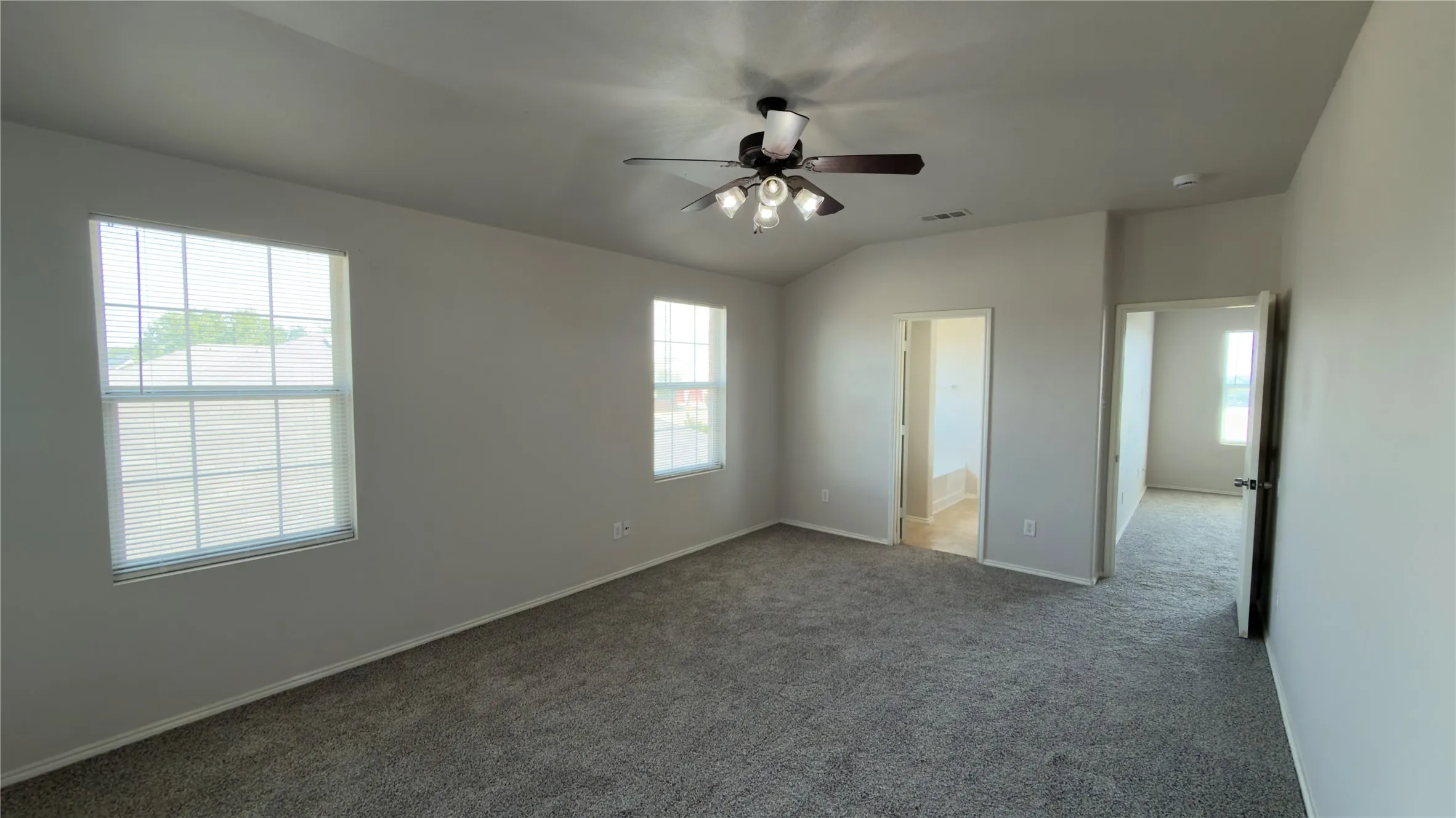 Vaulted ceiling with a ceiling fan, two windows with blinds, and gray carpet flooring
