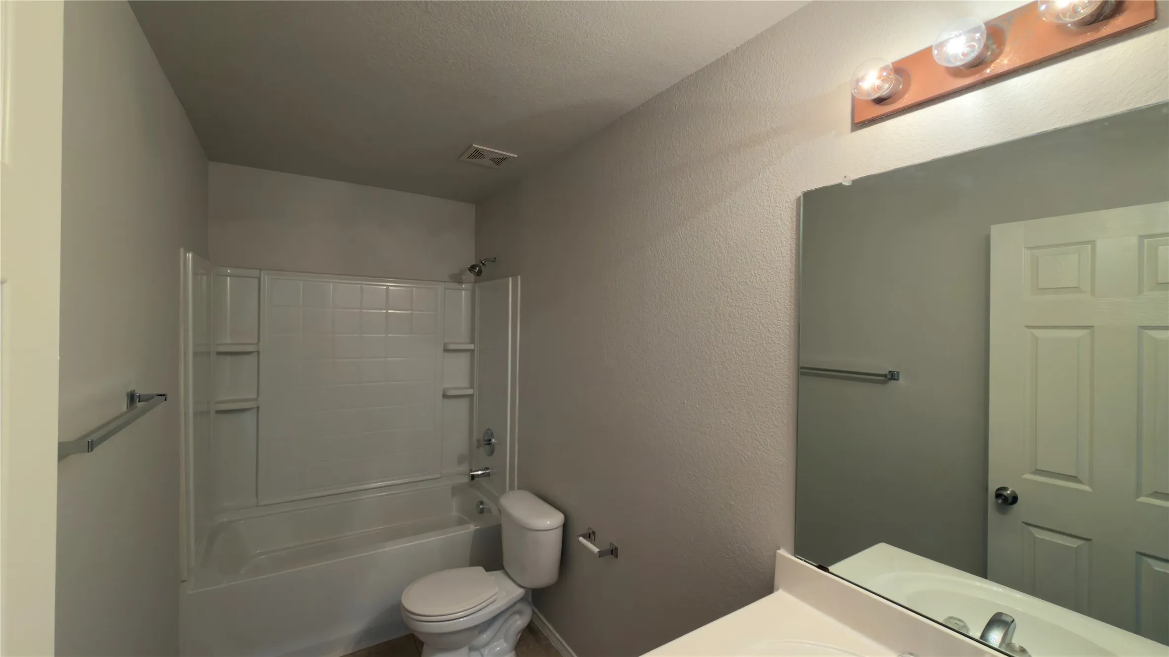 Tub/shower combination with white subway tile surround, white toilet, and vanity with integrated sink and chrome faucet