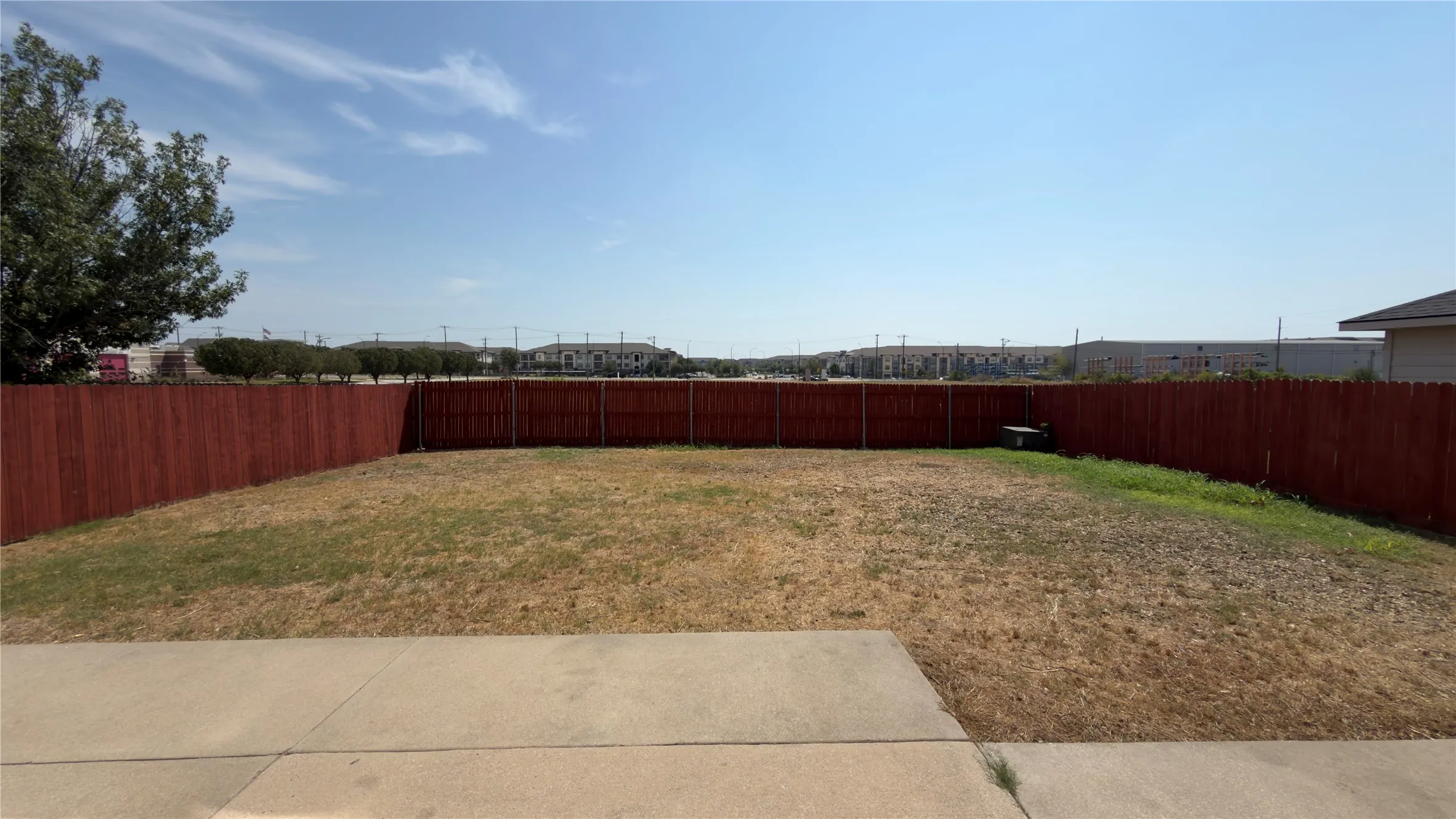 Expansive backyard area featuring a concrete patio, wood privacy fencing, and a generous grassy expanse