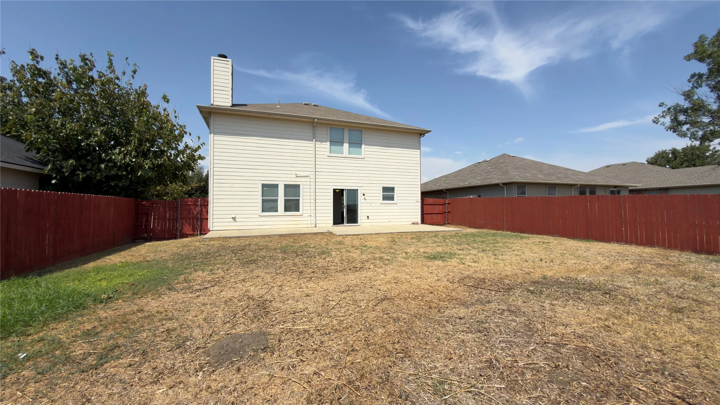 Expansive backyard featuring a concrete patio, full privacy fencing, and a two-story residence with horizontal siding