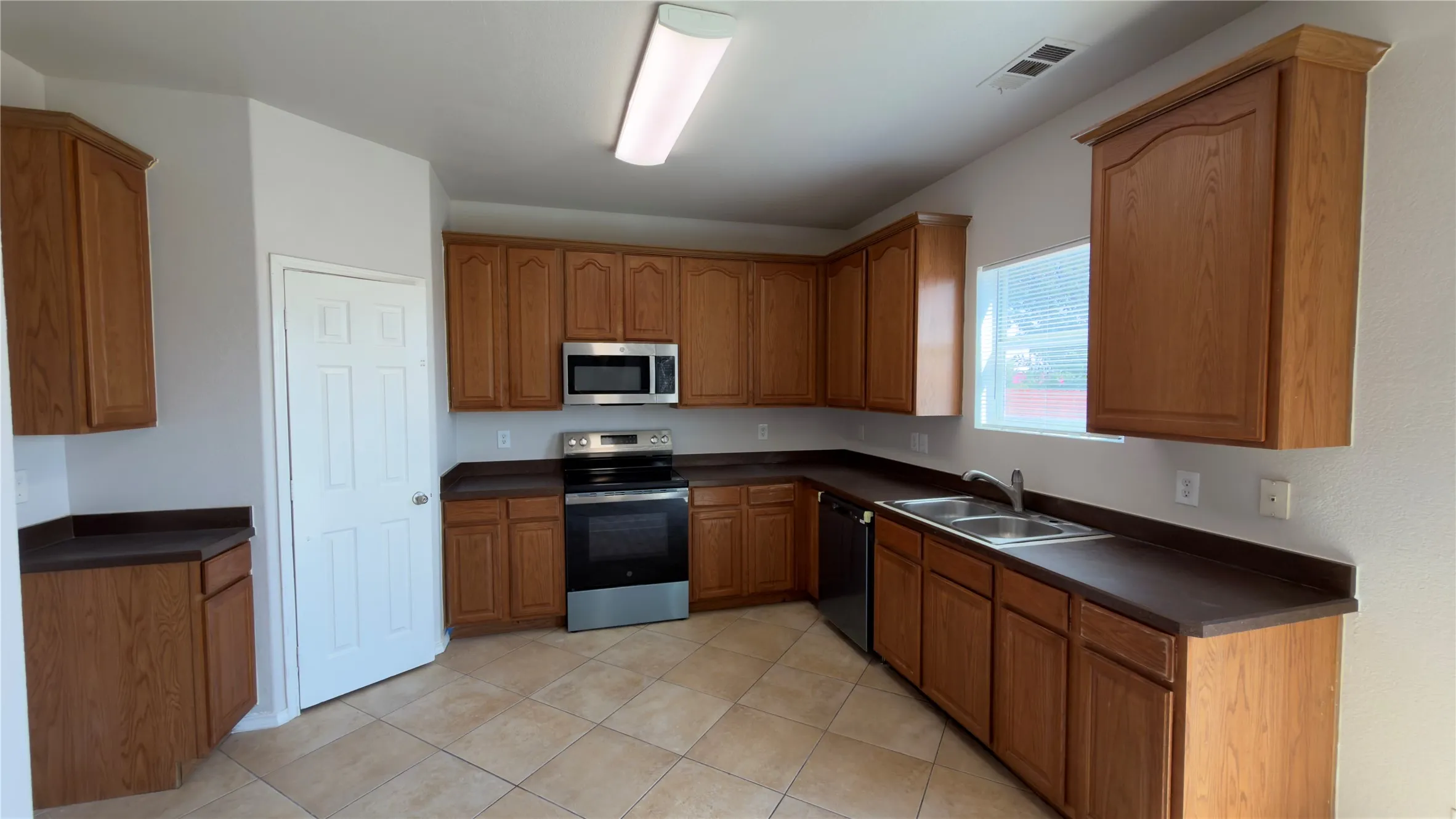 Expansive kitchen featuring wood cabinetry, stainless steel appliances, dual basin sink, durable countertops, and tile flooring