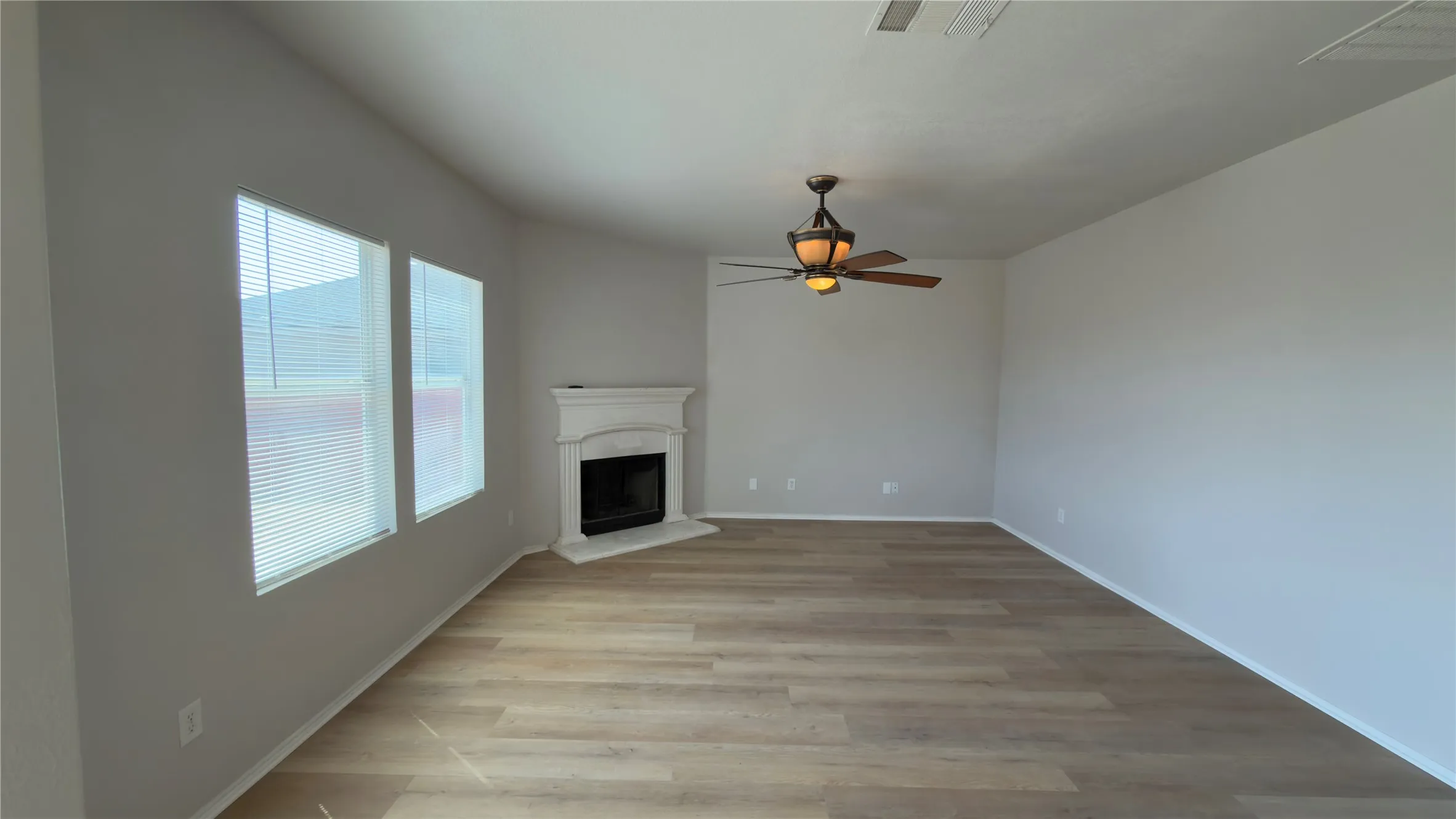 Living space featuring wood-finish flooring, two windows, a corner fireplace with decorative mantel, and a ceiling fan with integrated lighting