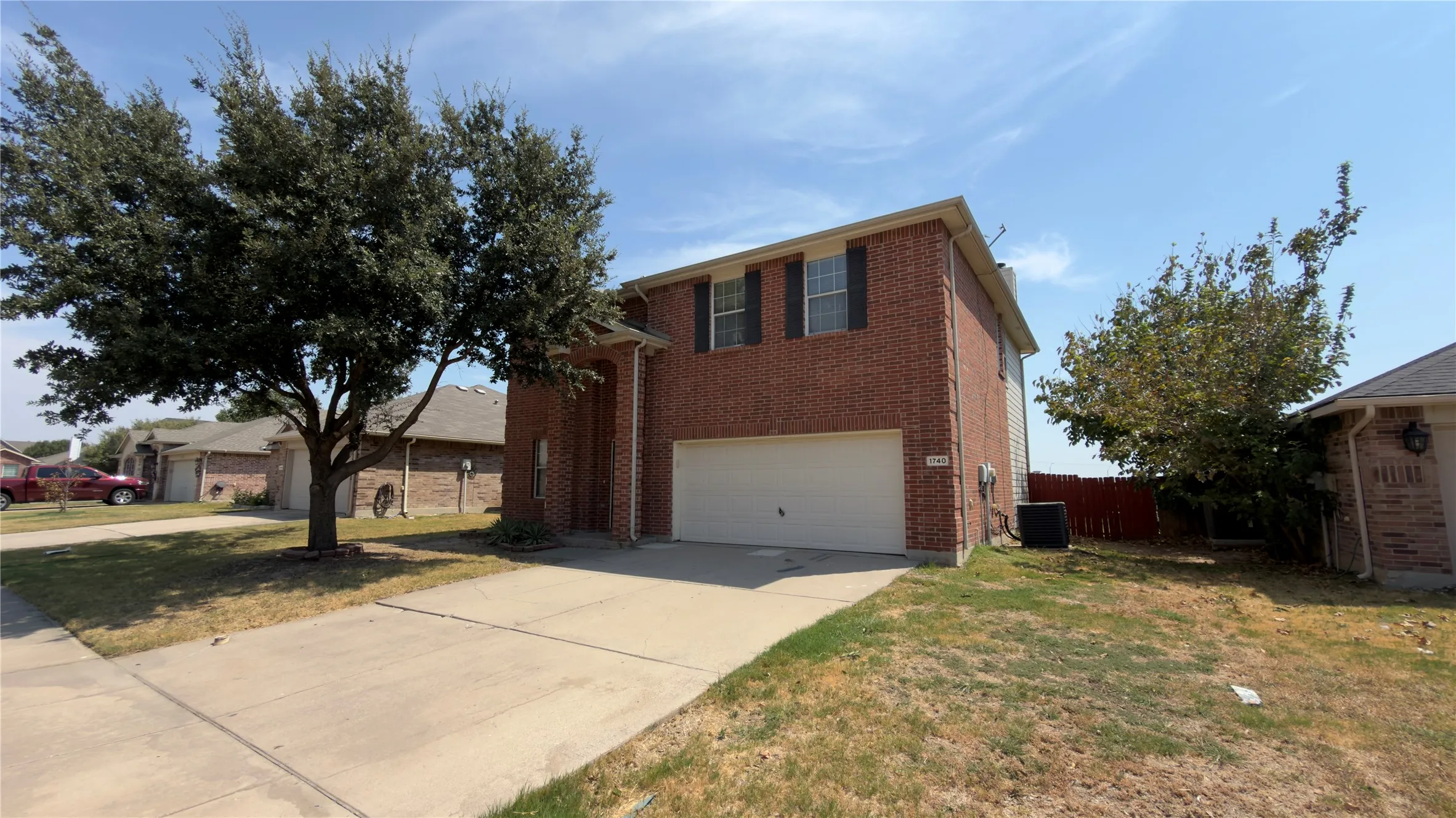 Brick exterior, two-story construction, attached garage, concrete driveway, and mature trees