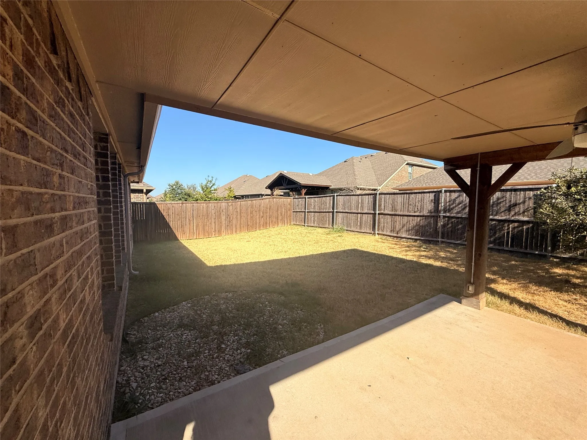 Covered patio with a ceiling fan, brick exterior, wood support beam, and a wood fence enclosing the yard