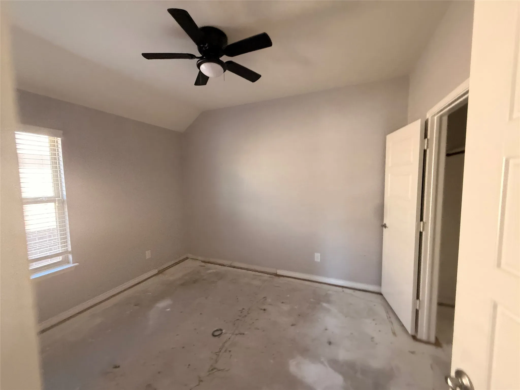 Vaulted ceiling, ceiling fan with integrated light, window with blinds, white paneled door, neutral wall paint