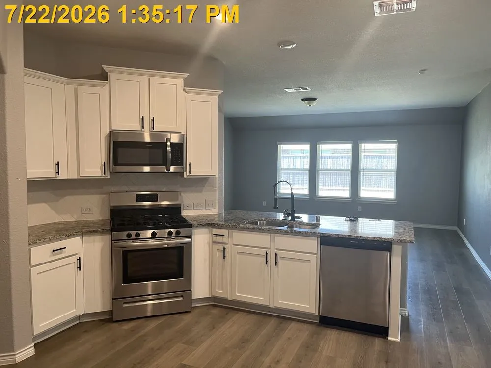 Kitchen featuring white cabinetry, stainless steel appliances, speckled countertops, and wood-finish flooring
