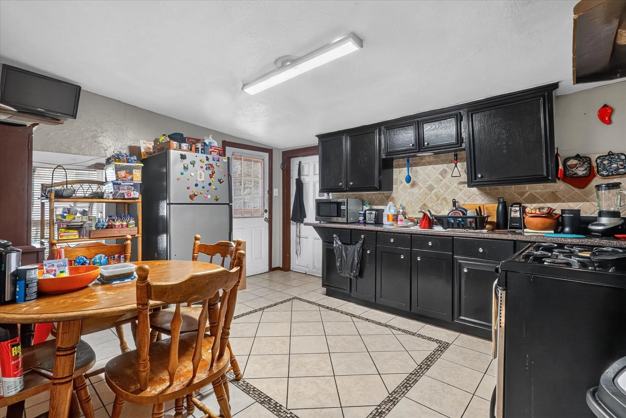 Kitchen featuring black cabinetry, tile flooring with decorative inlay, and a tile backsplash