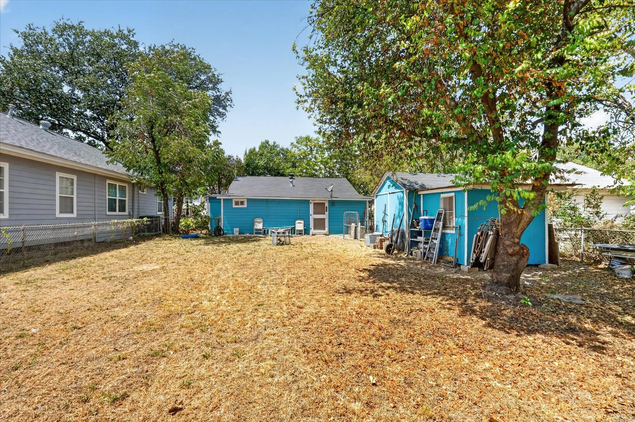 Yard with mature trees, offering a detached storage shed with a window and a secondary structure with blue siding