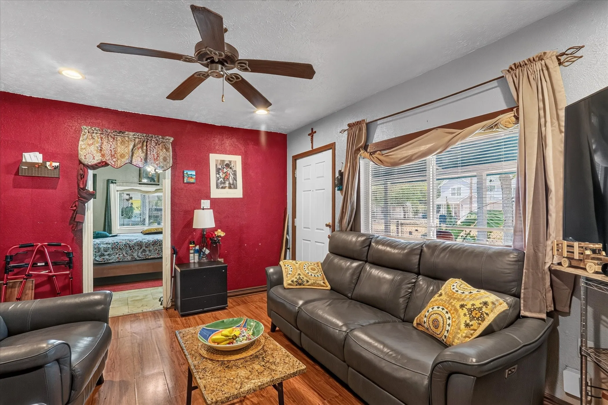 Wood-finish flooring, ceiling fan with integrated lighting, and a large window providing natural light
