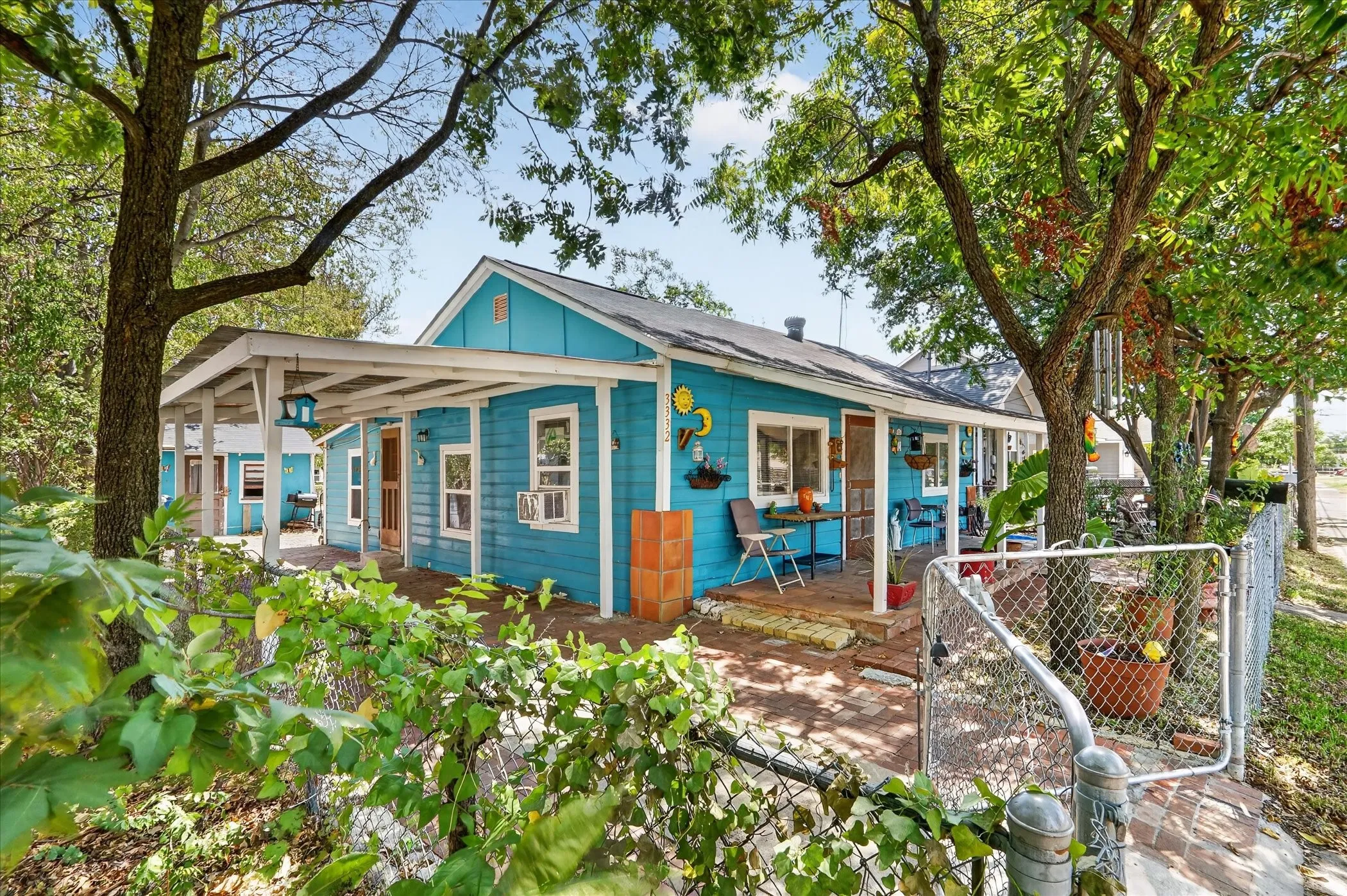 Turquoise siding, covered front porch, brick paver patio, wood-frame windows, and mature trees