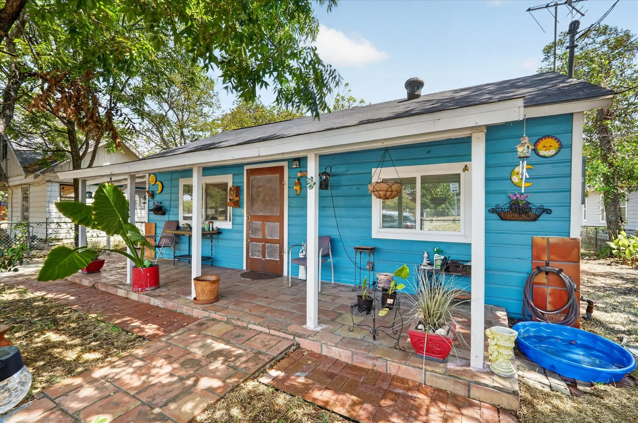 Single-story residence featuring blue siding, a covered porch with white columns, a dark shingle roof, and a red brick paver walkway