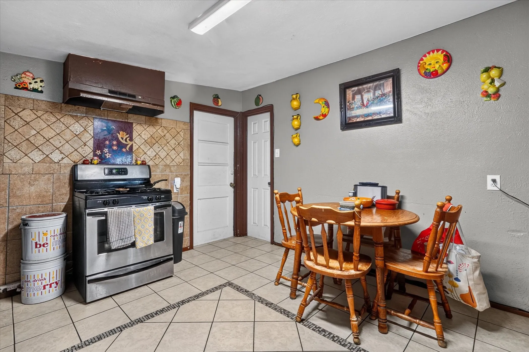 Tile flooring with decorative border, tile backsplash, stainless steel range, and a brown range hood