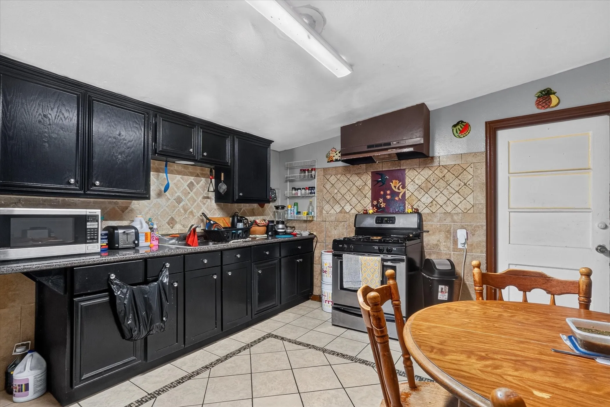 Kitchen featuring black cabinetry, light-toned tile flooring with decorative inlay, and a tile backsplash