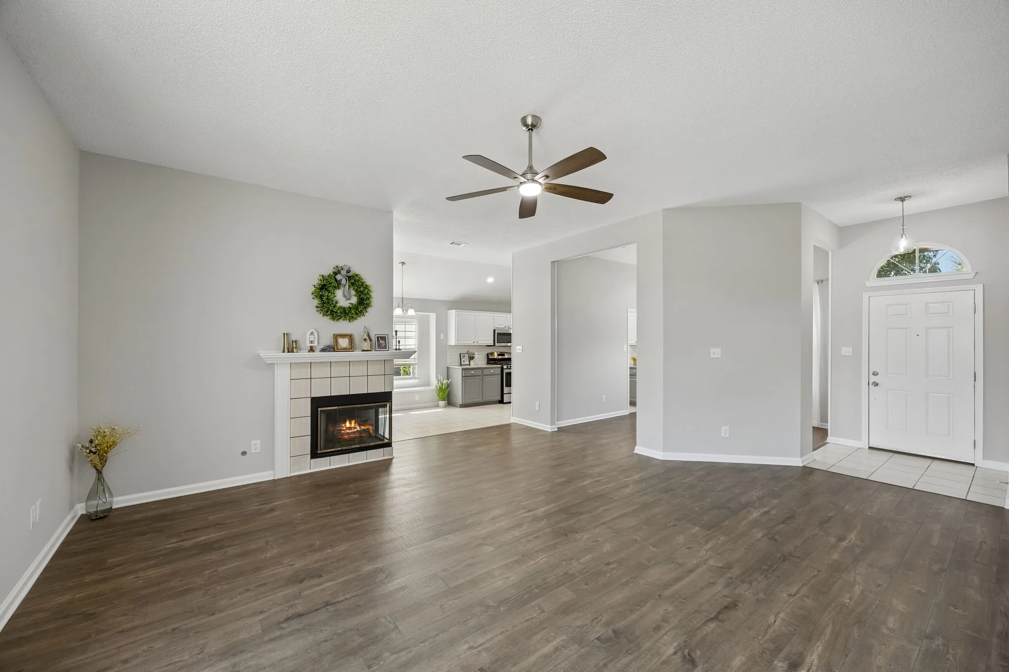 An open view of the main living area showcases neutral finishes, updated flooring, a cozy fireplace, and easy flow between the foyer, kitchen, breakfast area, and dining spaces.