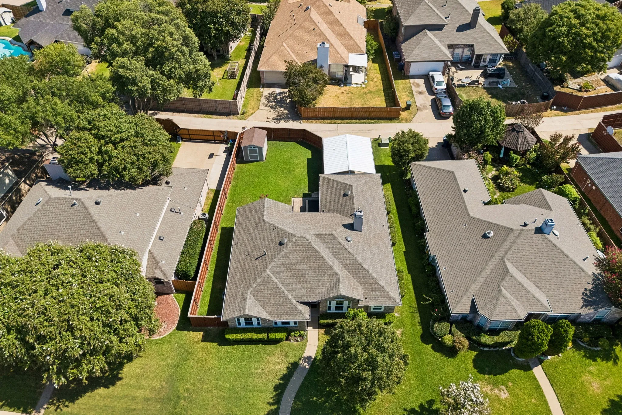 The aerial perspective beautifully illustrates the home's established setting, mature landscaping, fenced outdoor spaces, rear-access design, and generous covered parking.