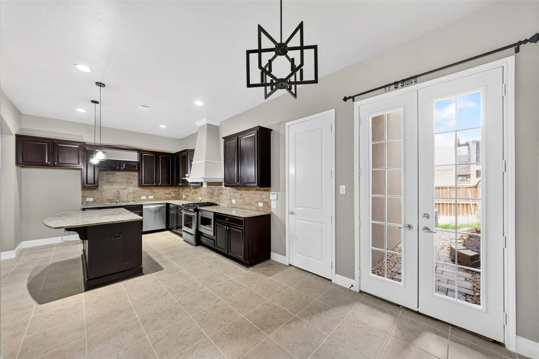 Expansive kitchen featuring dark wood cabinetry, stainless steel appliances, a center island with countertop, and tile flooring