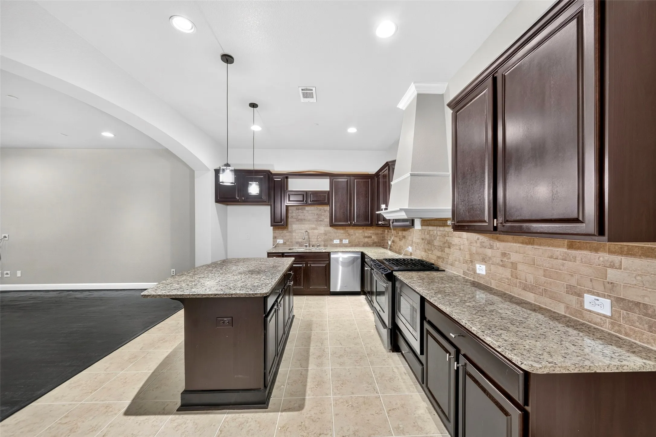Kitchen featuring dark wood-finish cabinetry, light-toned tile flooring, granite countertops, a tiled backsplash, and stainless steel appliances