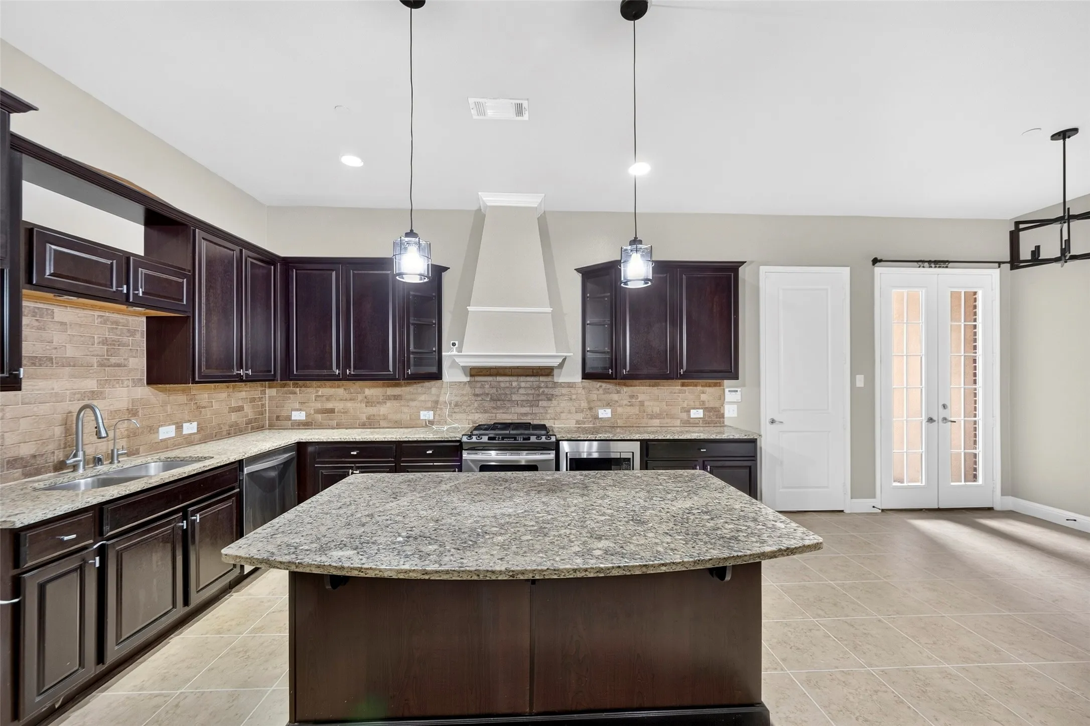 Spacious kitchen with dark wood-finish cabinetry, light-toned stone countertops, and a full-height tile backsplash