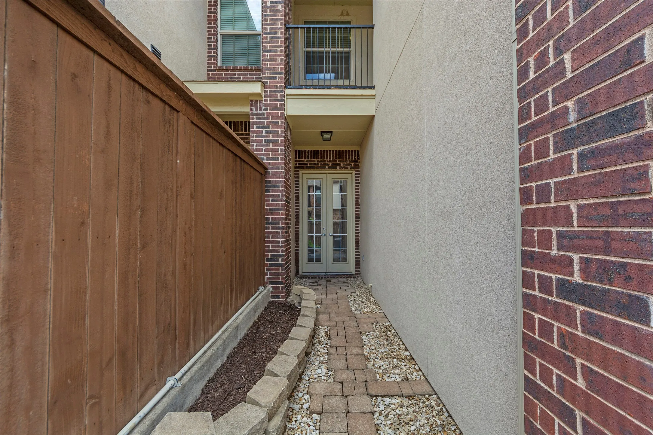 Private wood fence, brick exterior accents, stucco wall finish, paved stone pathway, and a glass-paneled entry door