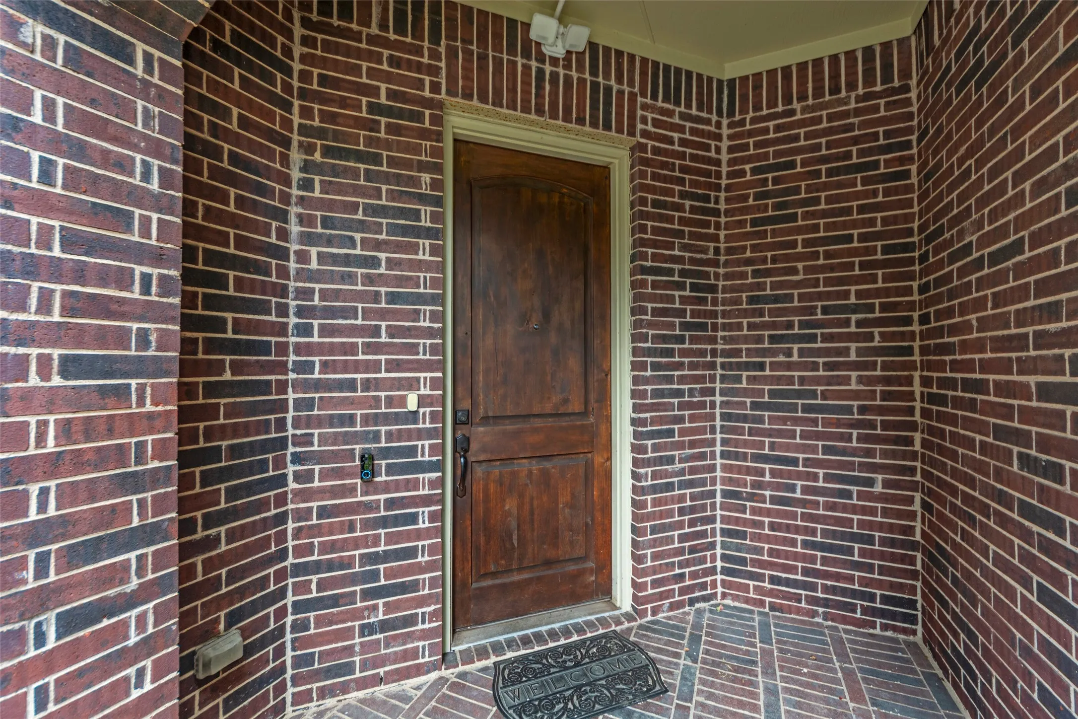 Rich brick exterior walls with a detailed wood entry door, complemented by light trim and a patterned brick floor