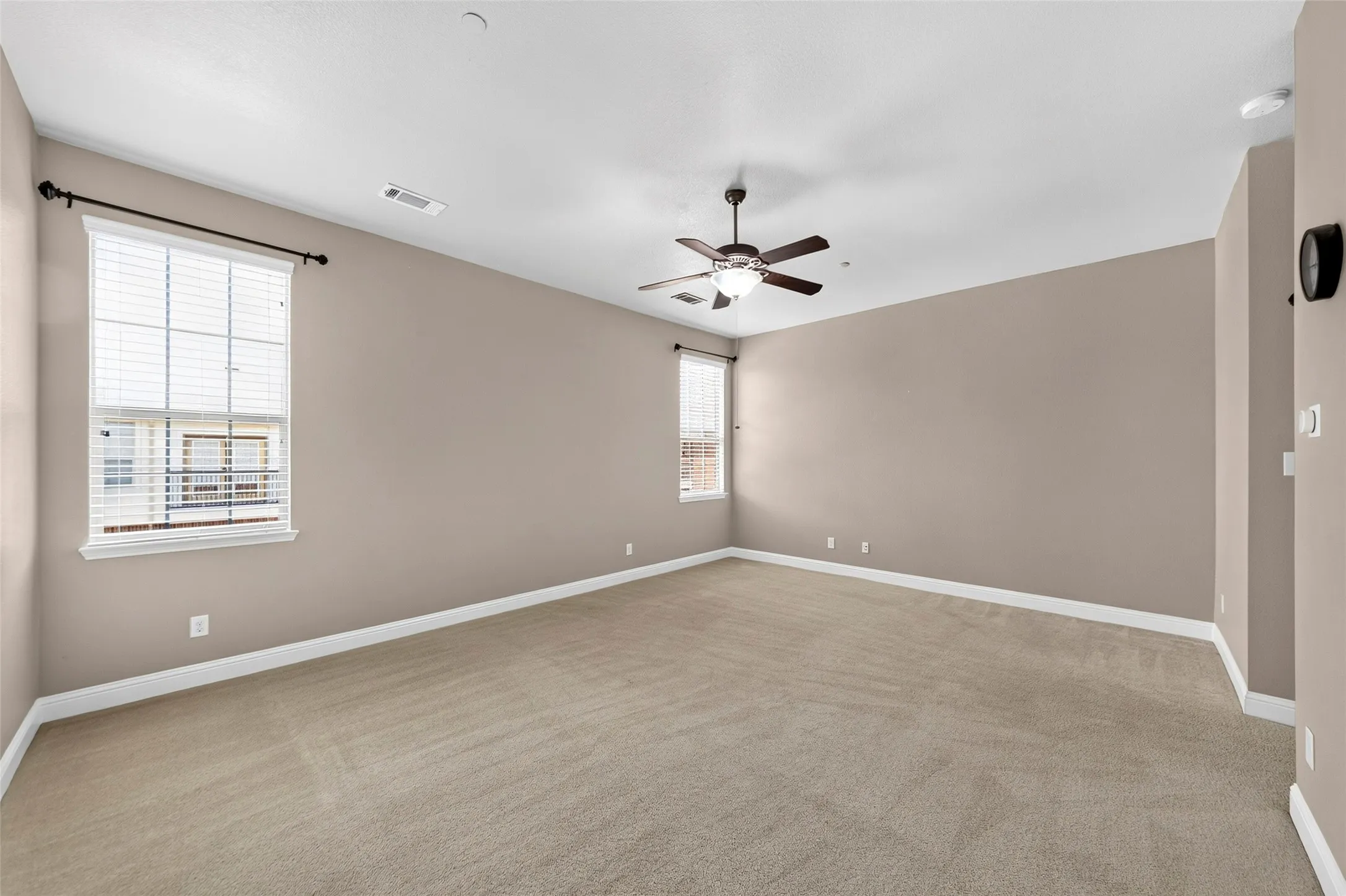 Spacious room featuring neutral carpeting, a ceiling fan with integrated lighting, and multiple windows providing natural illumination