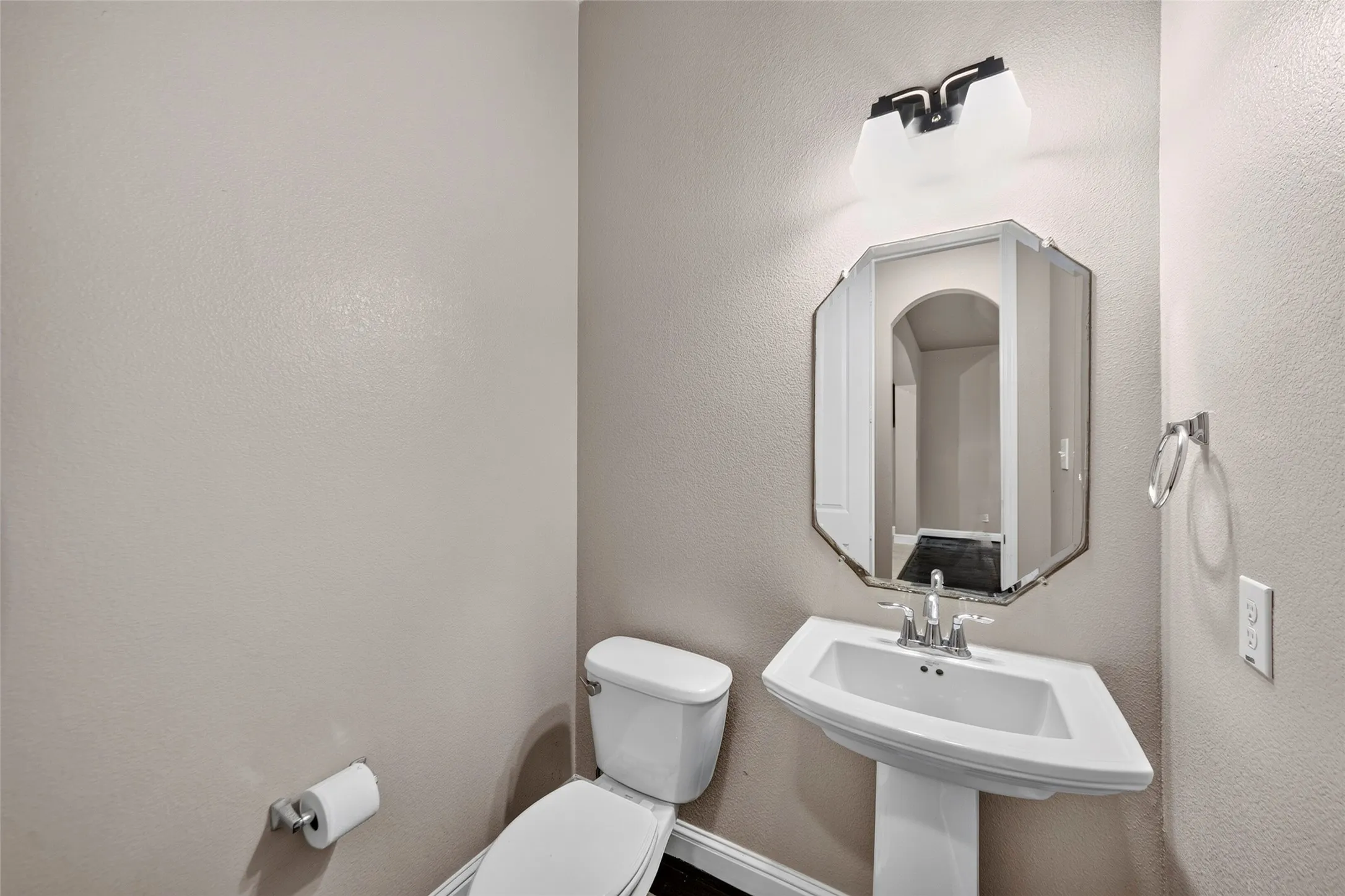 Pedestal sink with chrome-finish faucet, octagonal mirror, and overhead vanity lighting