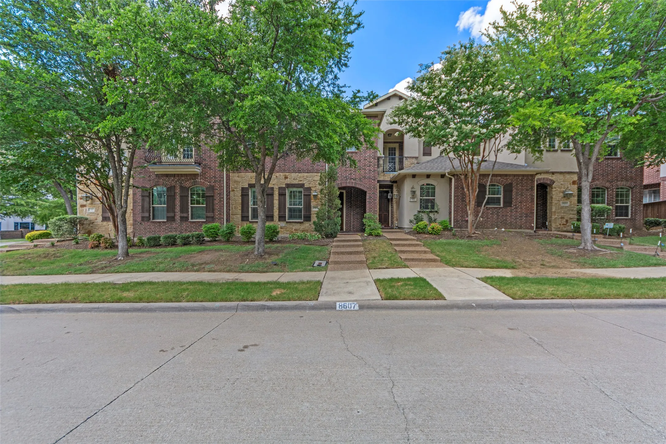 Brick and stucco exterior with multiple windows, arched entryway, and dark shutters